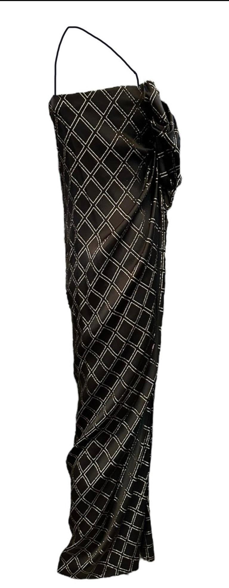 Découvrez le glamour et la sophistication des années 1970 avec cette superbe robe de James Galanos. Luxueuse en satin noir avec des fils d'or scintillants, cette robe dos nu à encolure en V est ornée d'un superbe nœud surdimensionné à l'encolure.
