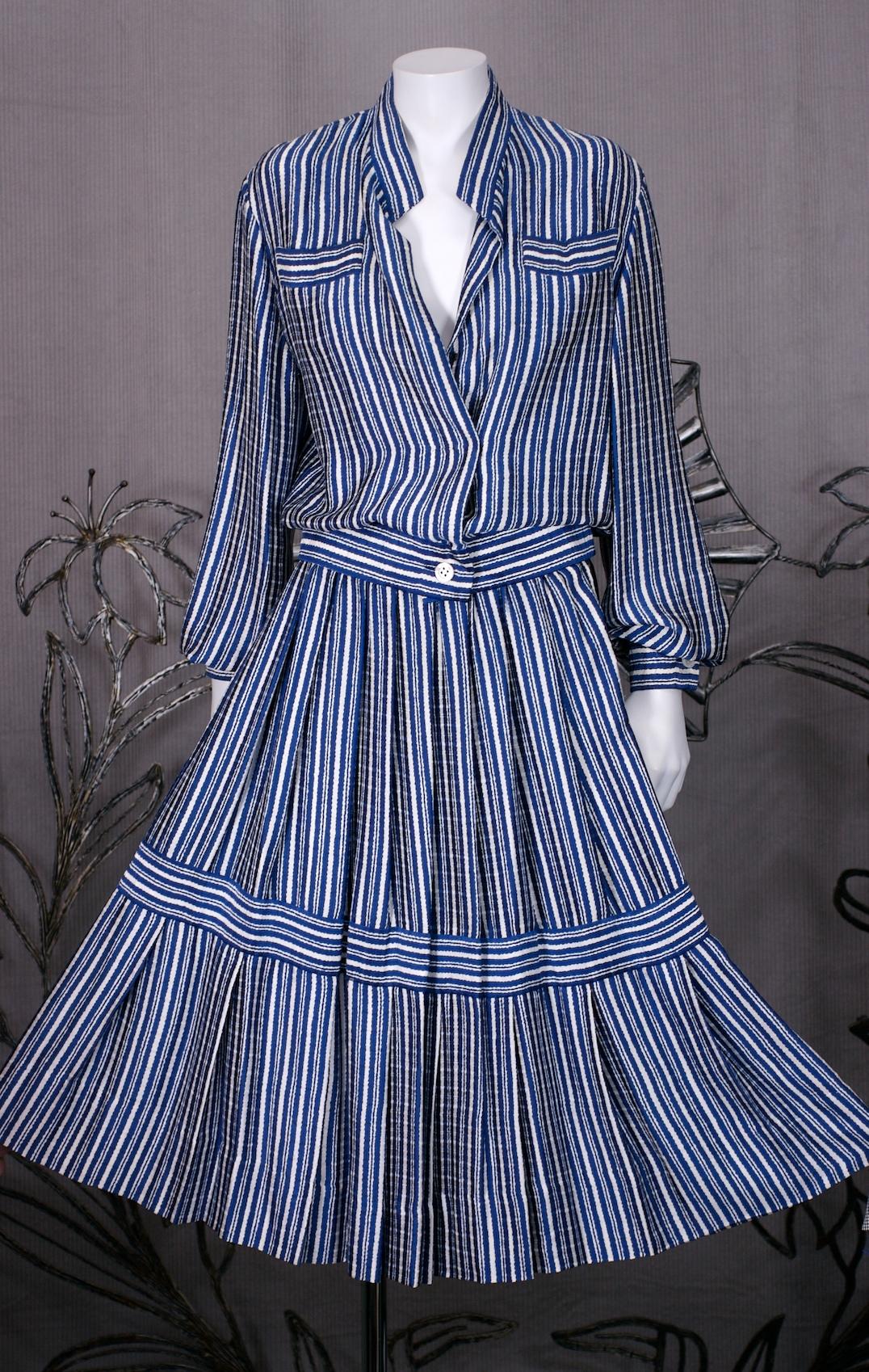 James Galanos Silk Crepe Striped 2 Pc Dress in printed silk crepe. Blue and white striped print is crafted into a blouson blouse and full pleated skirt. Covered front placket with mother of pearl buttons. Skirt is gathered at waist and a series of