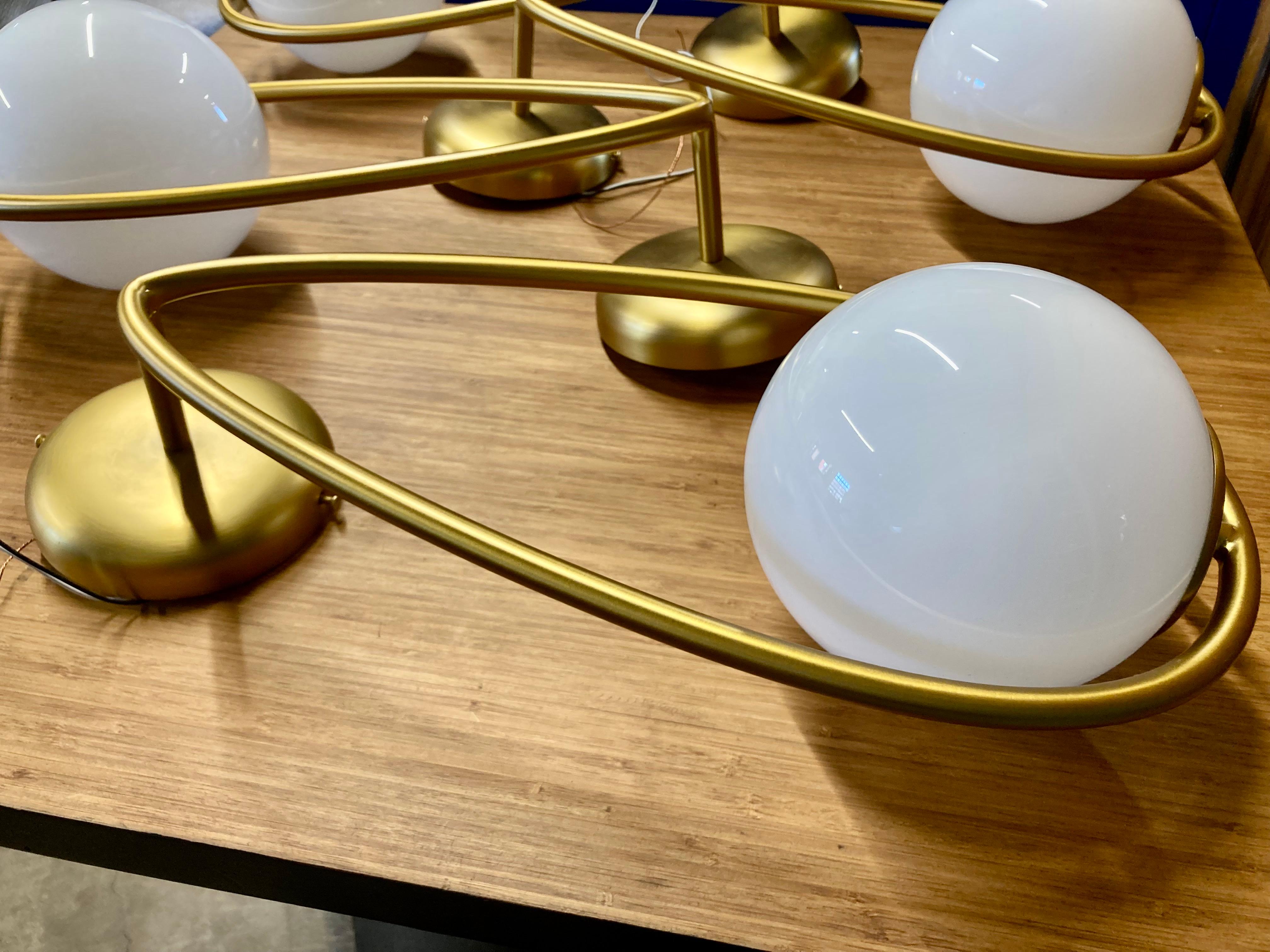 Applique inspirée d'une sculpture cinétique fabriquée par Visual Comfort. Le cadre est en acier avec une finition en laiton bruni. Les ampoules en verre au lait se vissent facilement dans le cadre. Vendu par lot de quatre. Voir la feuille