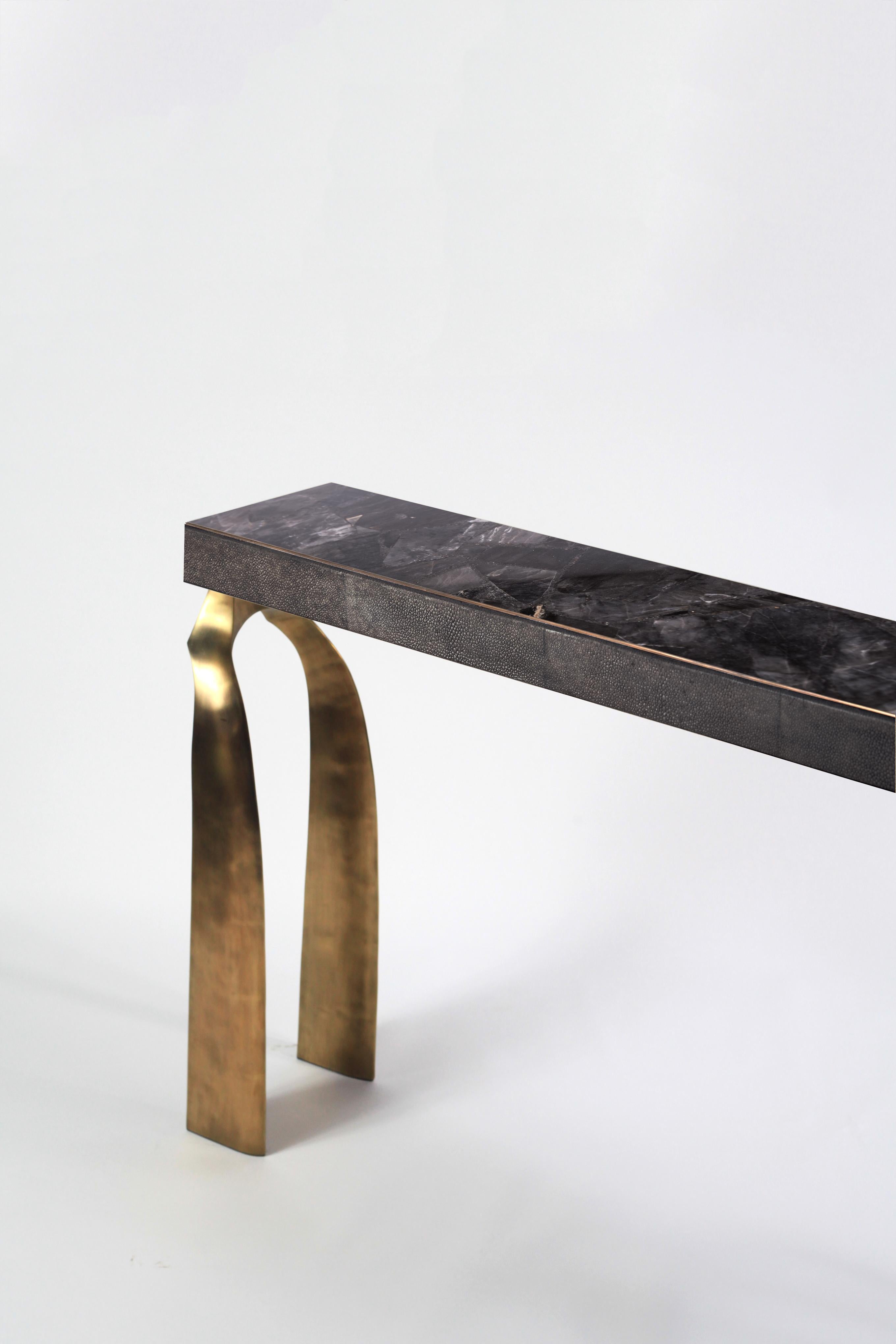 The Galaxy console table is both dramatic and organic it’s unique design. The black quartz top, with coal black shagreen inlaid borders, sits on a pair of ethereal and sculptural bronze-patina brass legs. This console table comes in different