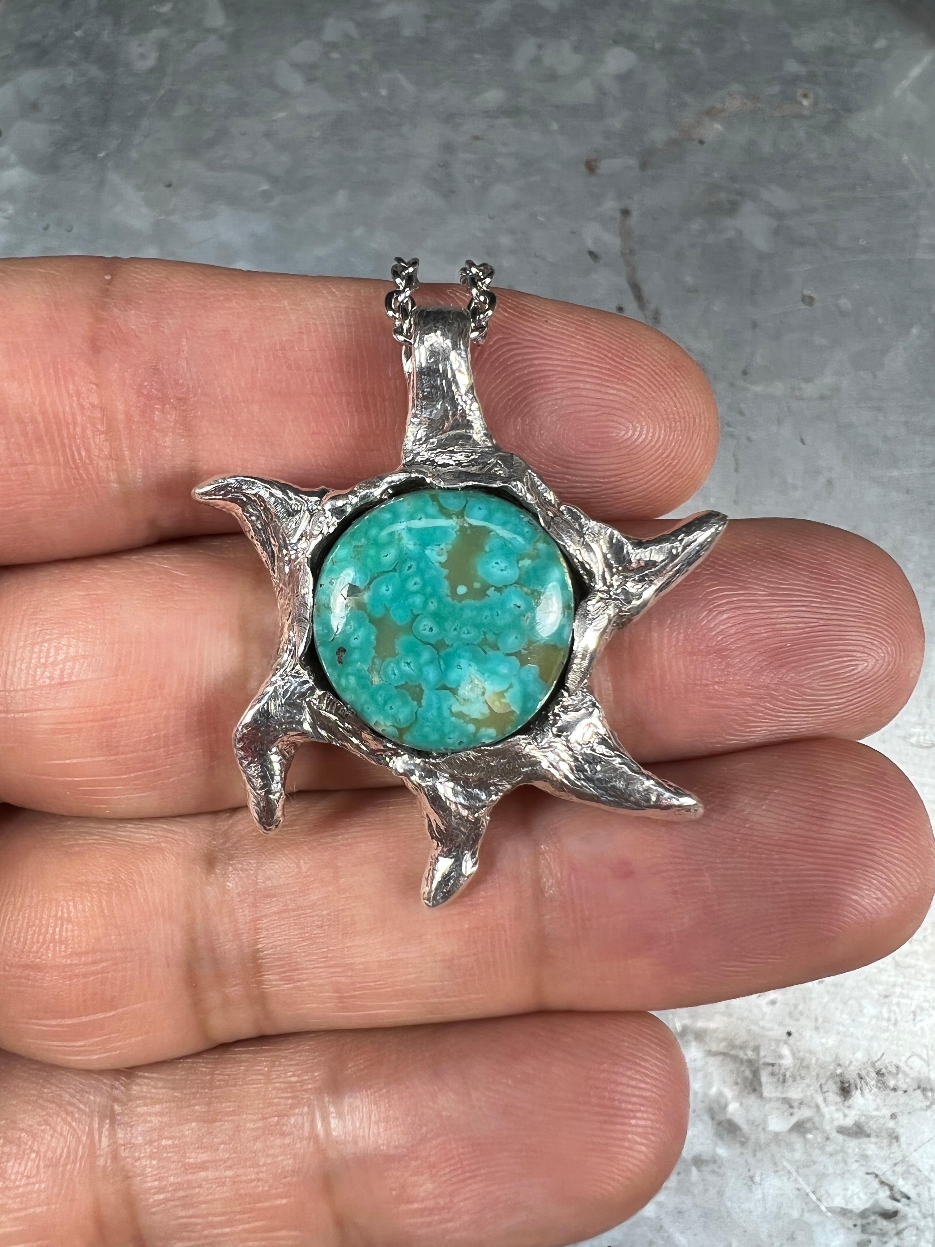 This one-of-a-kind pendant is meticulously hand-carved and cast in sterling silver and features a stunning Manassa Turquoise stone from Colorado. The stone is a perfect complement to the intricate silverwork that depicts the celestial wonder of a