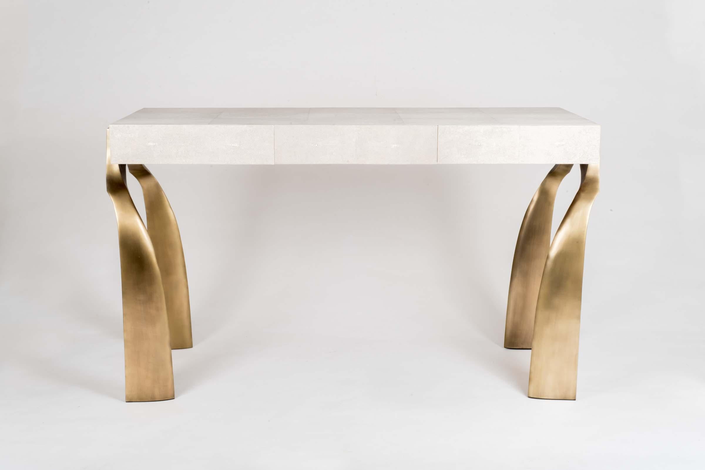 The Galaxy writing desk in cream shagreen, is a classic and sculptural piece with its beautifully shaped bronze-patina brass legs. This piece has three wood-veneer drawers, add a mirror and this desk becomes a vanity. The shagreen is hand-dyed by