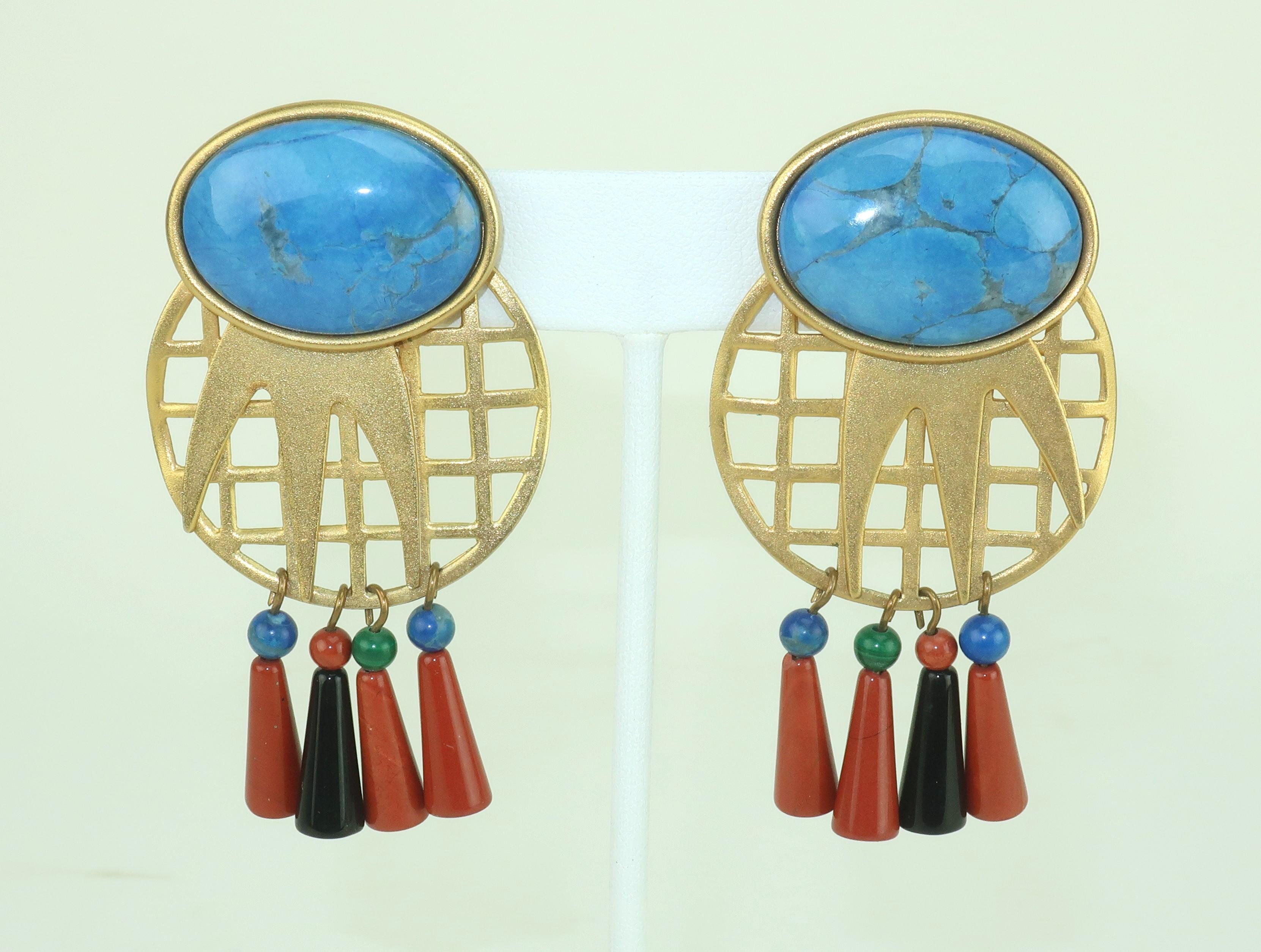 Post modern perfection! A pair of matte gold metal earrings with a turquoise blue stone embellishing a grid with dangles in turquoise blue, jasper brick red, malachite green and onyx black semi precious stones. Outfitted with clip-on hardware. These