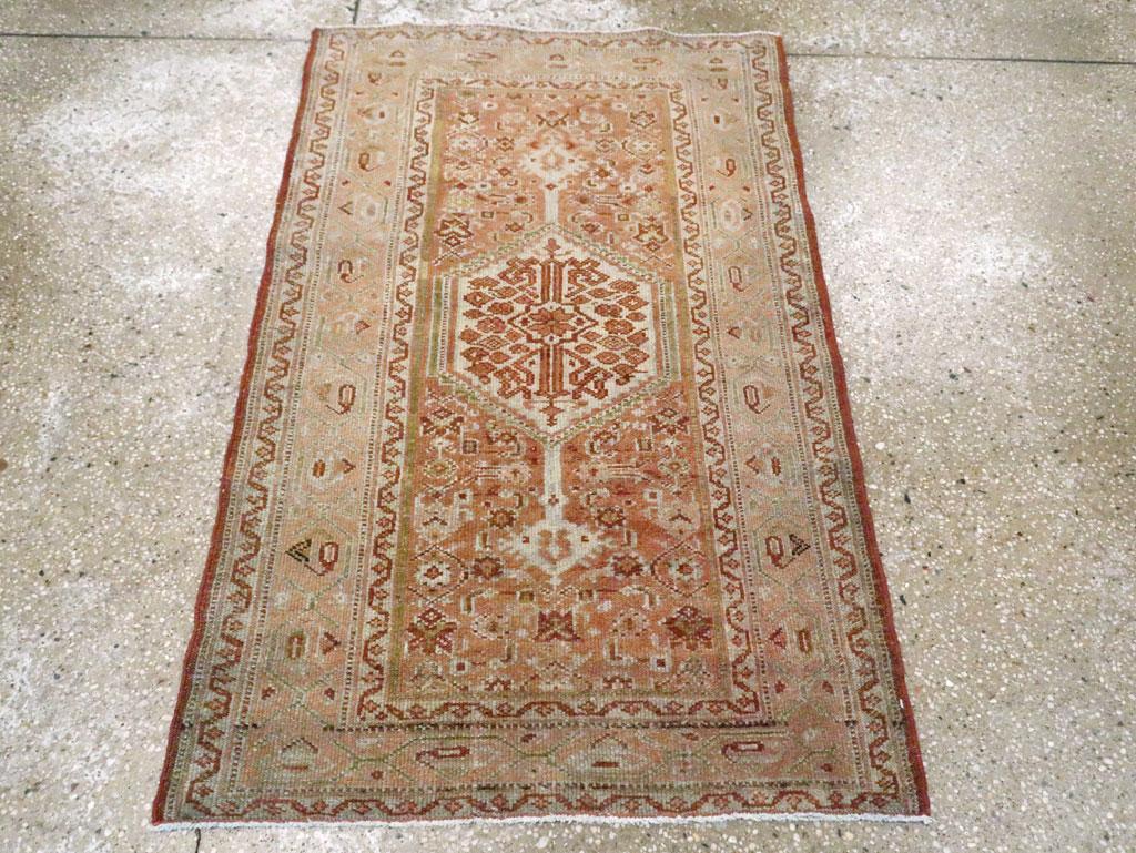 Esta alfombra persa Malayer de mediados del siglo XX, de 1,8 m x 1,8 m, presenta un diseño equilibrado y simétrico que se distingue por su medallón hexagonal central. El medallón, colocado sobre un cálido campo de terracota, está lleno de una