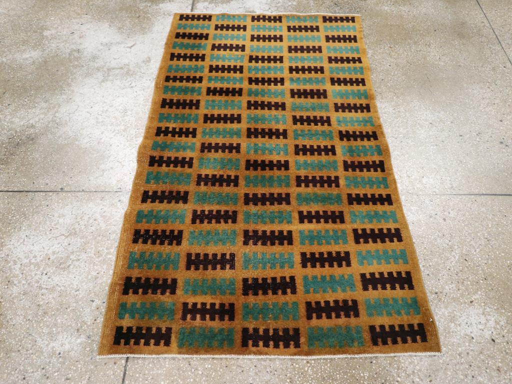 Esta alfombra deco turca de Anatolia de mediados del siglo XX, que mide 1,80 x 1,80 m, presenta una composición audaz y minimalista con motivos horizontales repetitivos dispuestos en forma de cuadrícula. Sobre un fondo ocre dorado, las filas