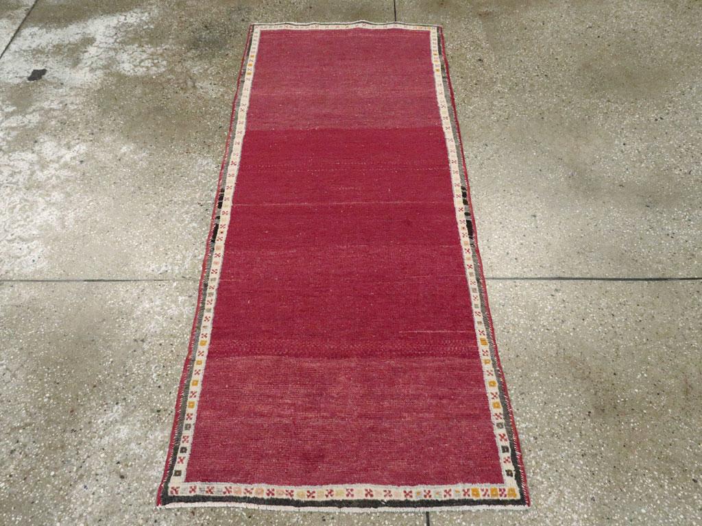 Ein türkisch-anatolischer Teppich im Vintage-Stil. Eine schnurartige elfenbeinfarbene Bordüre bildet einen einfachen Rahmen für das gut abgetragene, völlig schlichte scharlachrote Feld dieses mitteltürkischen Dorfstreus. Der Look ist modern oder