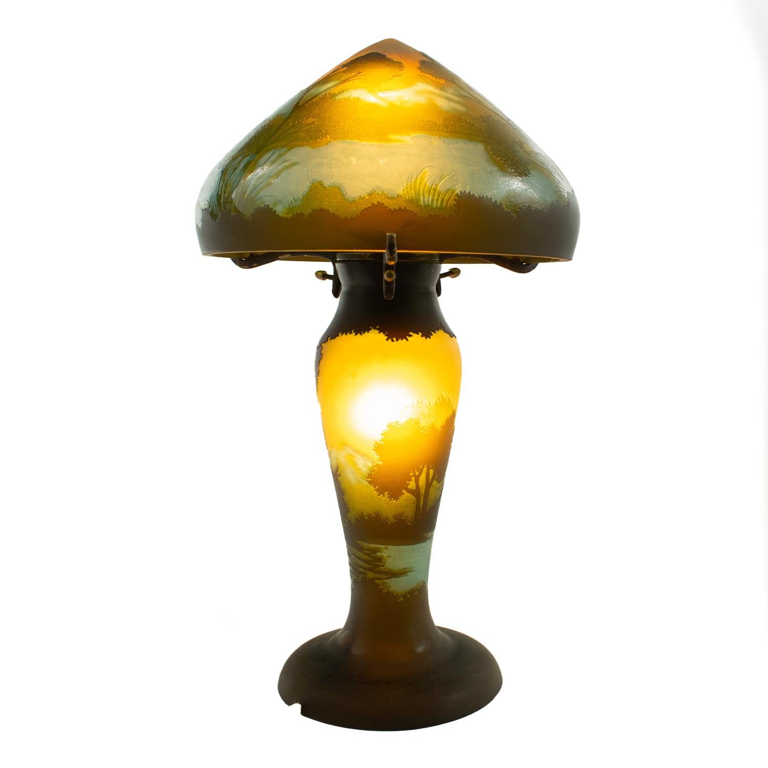 Établissement Gallé, lampe champignon Art nouveau en verre multicouche à décor de paysage gravé à l'acide dans les bleus, les verts et les jaunes. Signé Gallé.
Dimensions : h. 36cm

La lampe est en état de marche et le câblage d'origine a été laissé