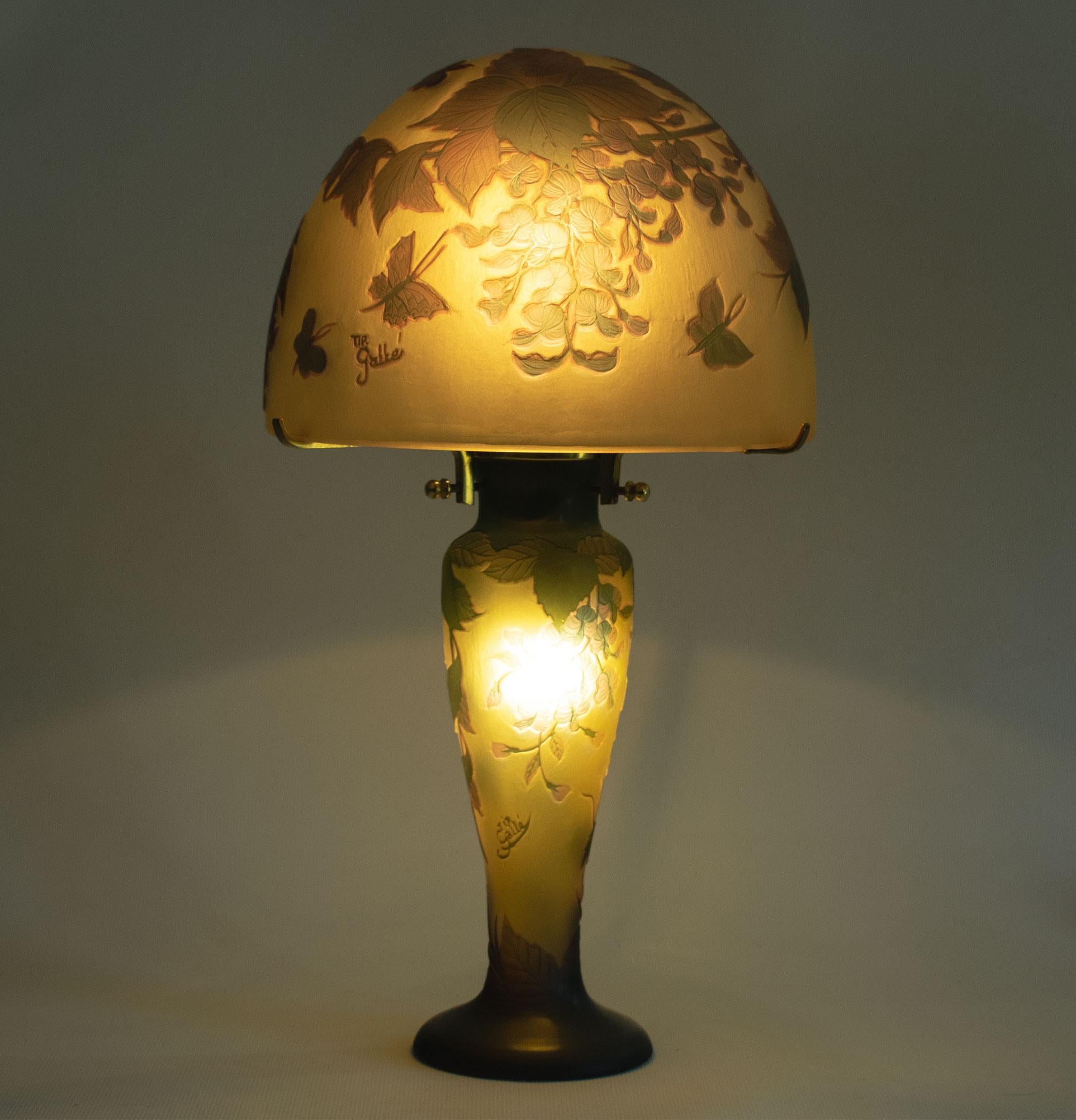 GALLÉ Tip - Elegant Art Nouveau mushroom lamp in acid-etched glass decorated with wisteria and butterflies in muted tones of violet and green on an ochre background. Height. 35cm. Diameter of lampshade: 19 cm. 

Lamp signed “Gallé”, accompanied by a