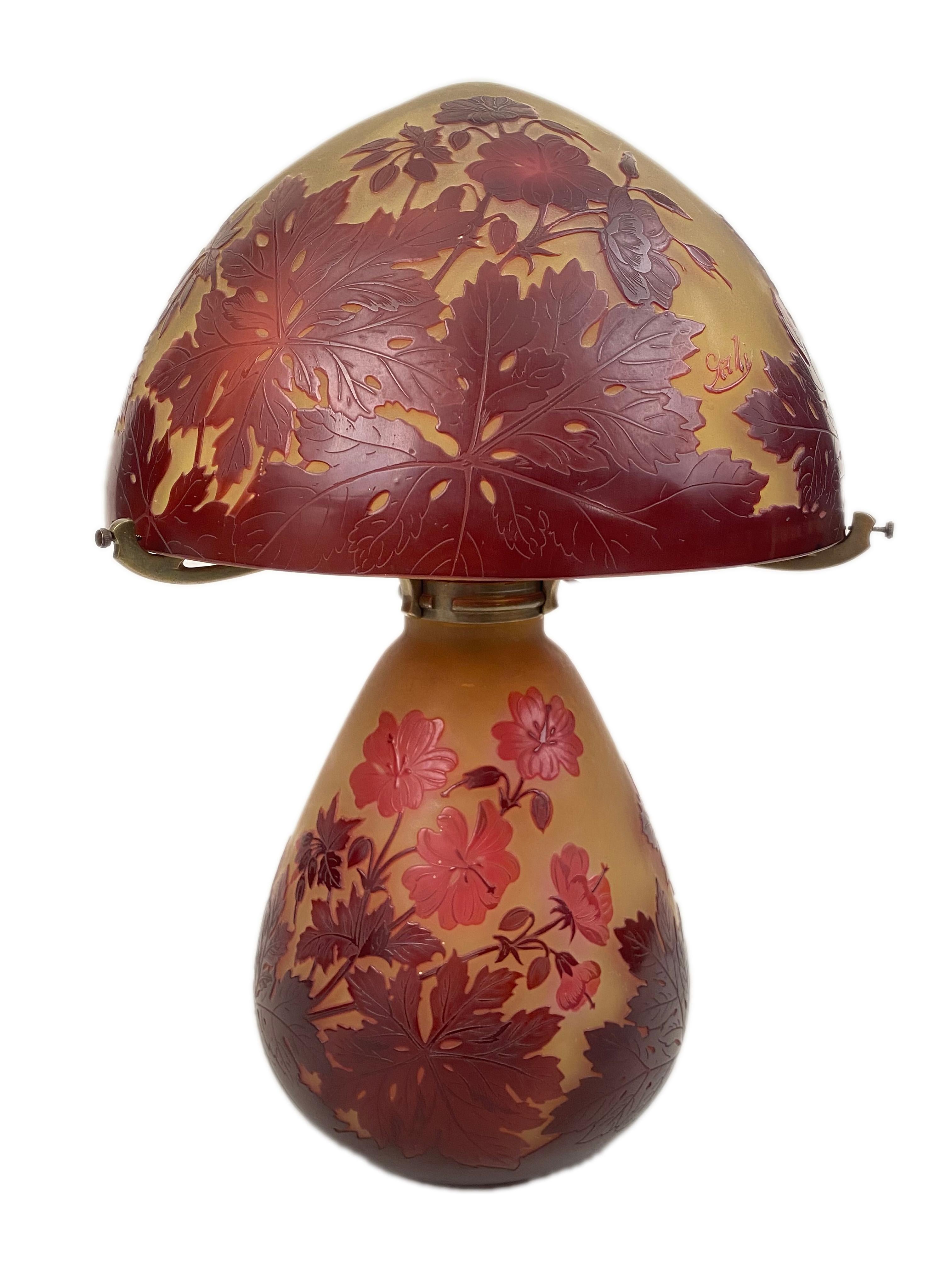 An early 20th century French Art Nouveau cameo and bronze glass table lamp by, Emile Gallé with both base and shade decorated with all over vibrant, crimson red flower, leaf and stem decoration against a yellow - white background. Both the base and