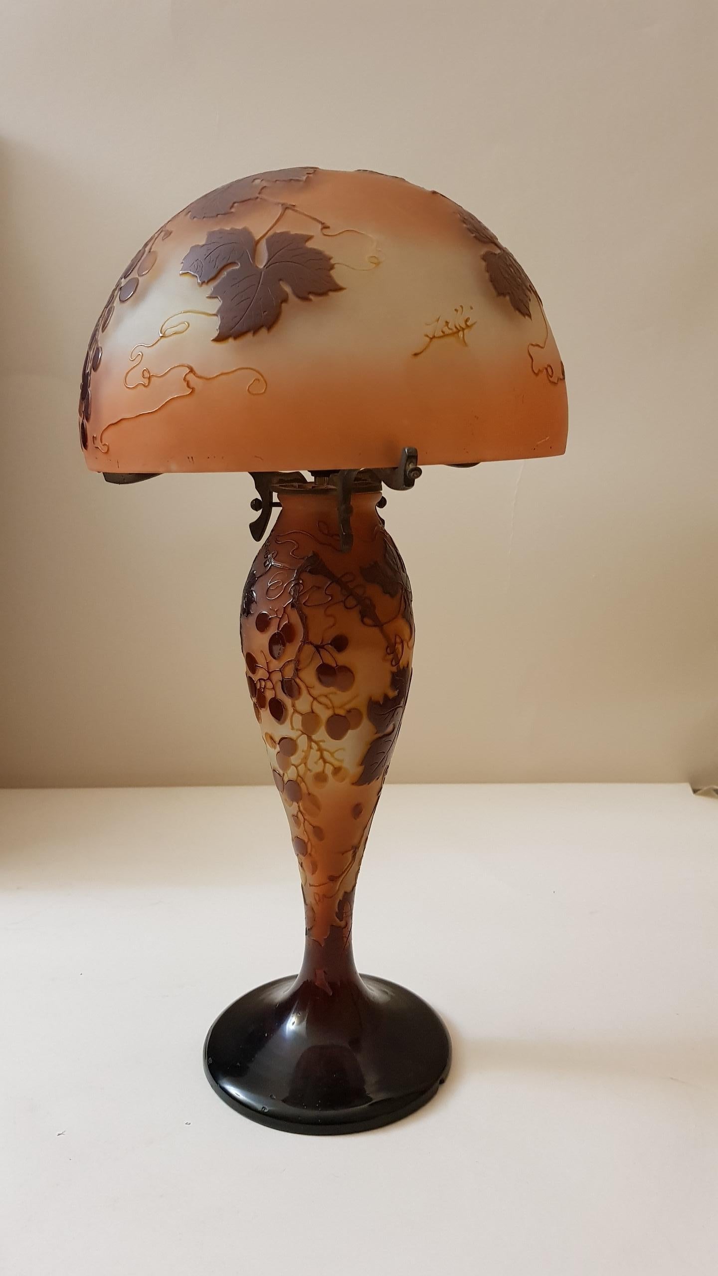 LAMP WITH PAMPRES OF VINE in multilayer glass with shaped hat
mushroom, baluster shaped foot and gilded bronze mount with three branches.
Decorated with acid vines of vines in brown on a background of shades of purple.
Signed cameo on the foot and