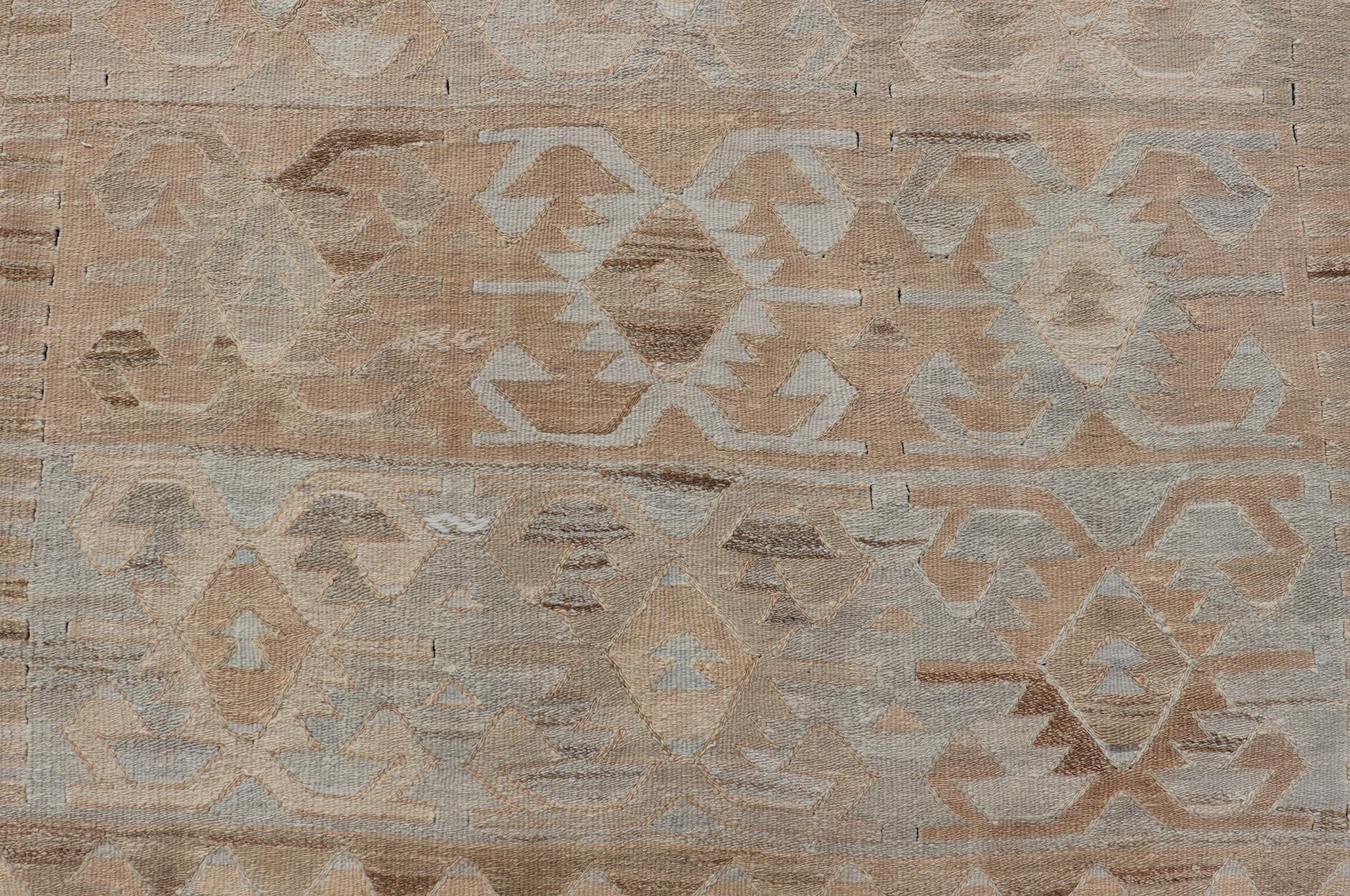 Measures: 5 x 10'1 

This vintage Turkish flat weave Kilim features tribal relics and faded earthy neutrals. The repeating design covers the entire field of muted light blue, caramel, taupe and gray. The border is a tribal saw-tooth design