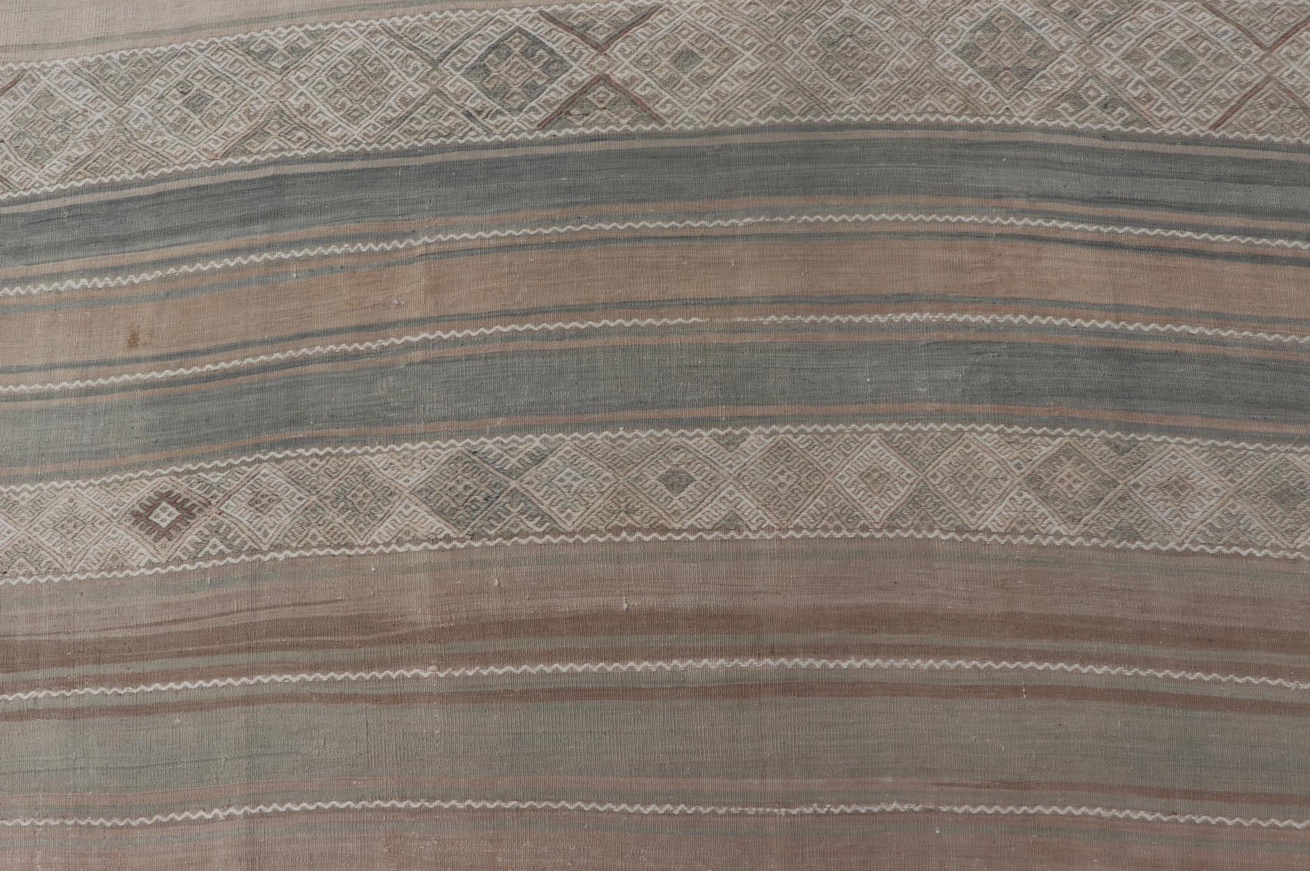 Measures: 6'10 x 14'7 

This vintage Kilim features simple design, stripes panel with stylized embroidered pattern. Rendered in muted shades of tan, taupe, light green, and faded blue makes this piece is charming. 

Country of Origin: Turkey;