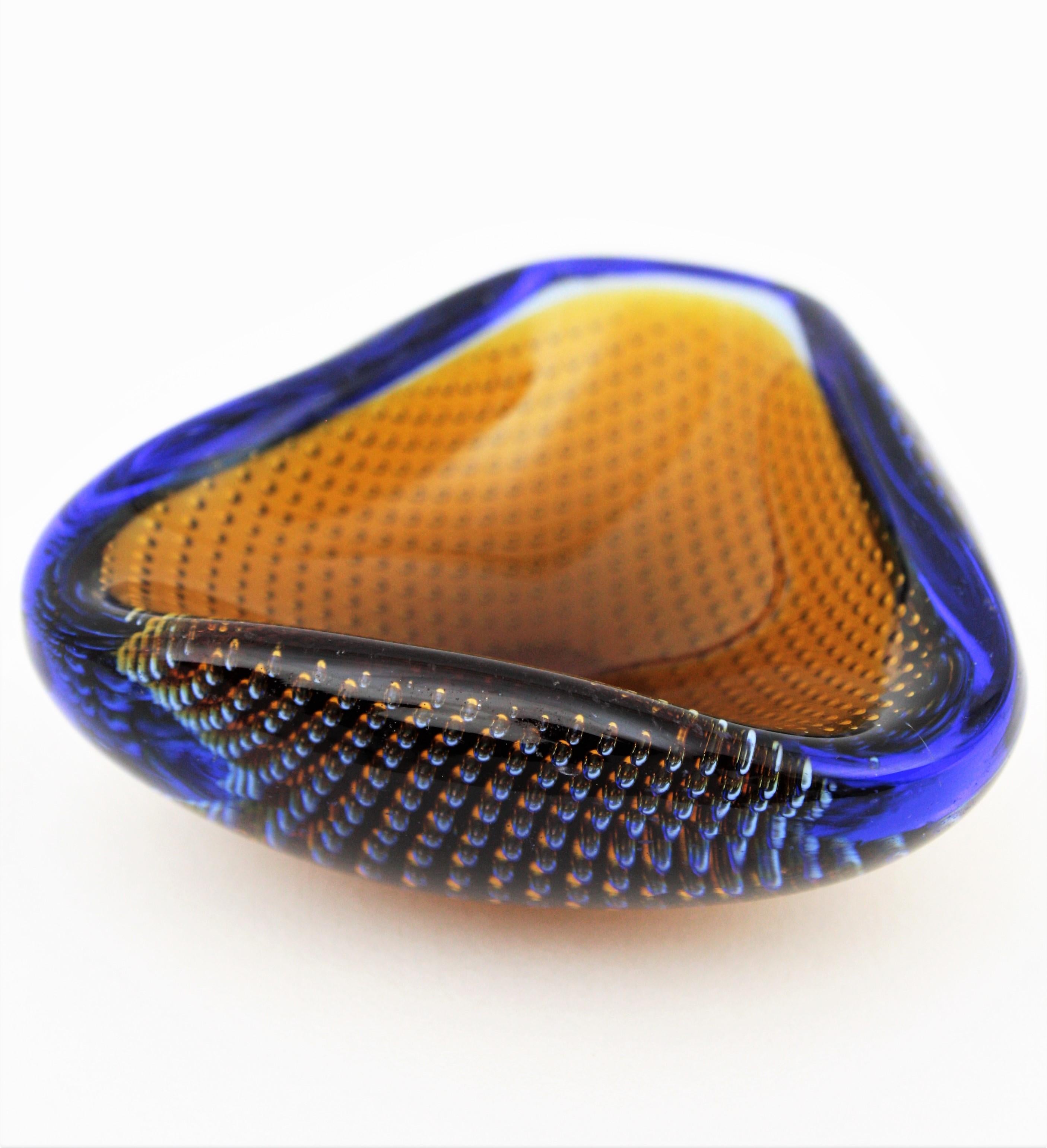 Triangular shaped hand blown murano glass geode bowl with inner controlled bubbles attributed to Galliano Ferro. Italy, 1960s.
Made in amber and klein blue glass cased into clear glass with the Sommerso technique.
Lovely to be used as rings bowl