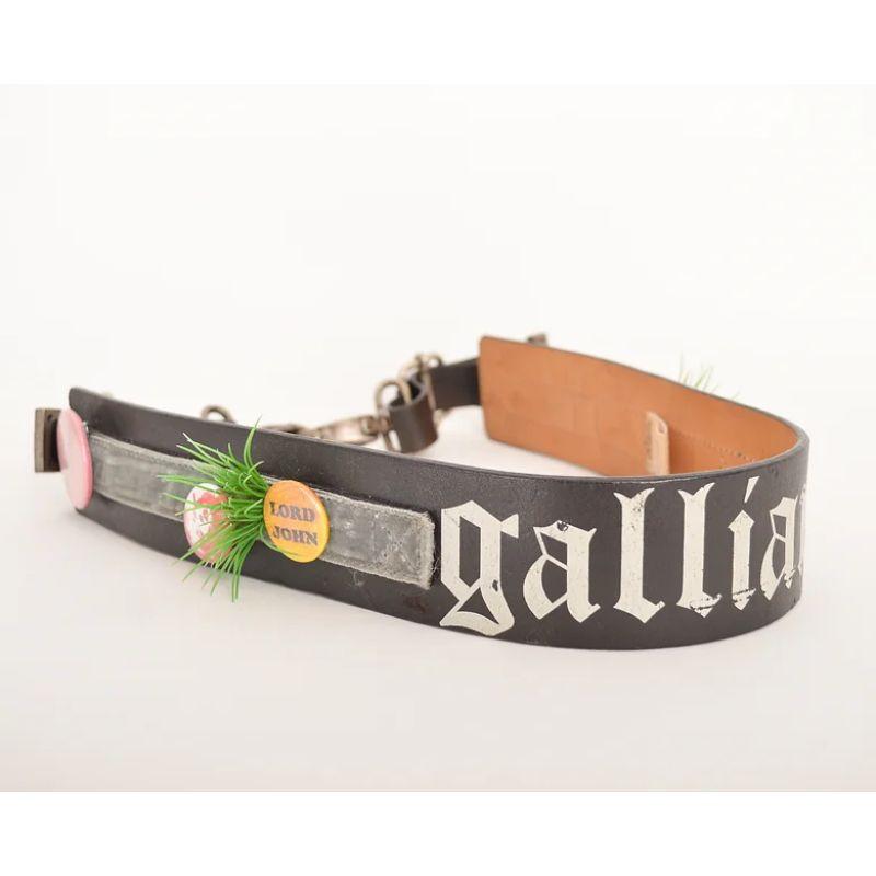 Early 2000's John Galliano waist belt, with the iconic & gothic 'Galliano' branding. 

Features silver velvet ribbon, removable decorative pin badges and garish fake grass embellishment. The belt fastens via a heavy, silver tone metal buckle clasp