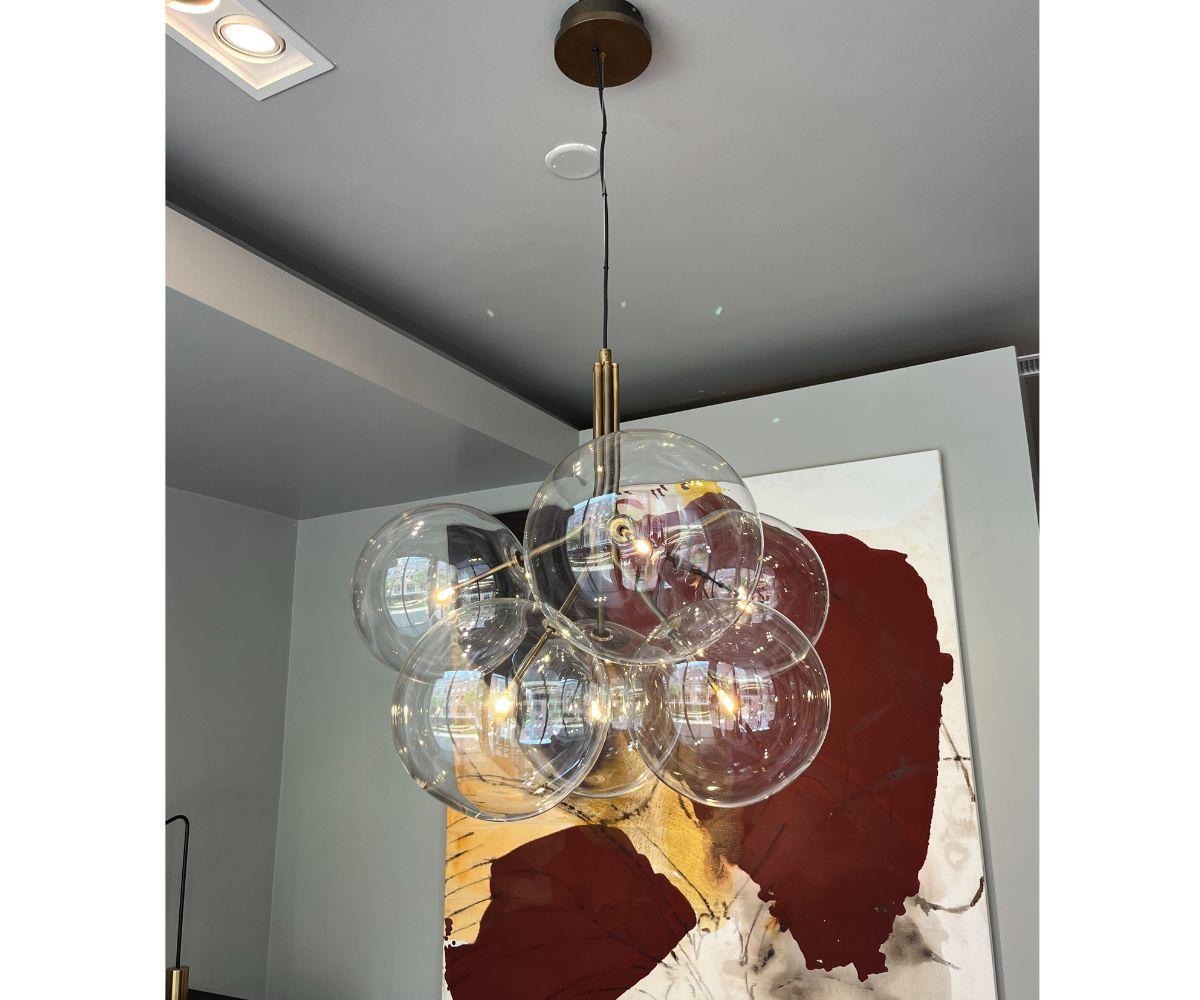 The Gallotti&Radice Bolle Hanging Lamp, designed by Massimo Castagna, features six transparent mouth-blown glass spheres and a hand-burnished brass structure. With a total fixture height of 54 inches, this elegant lamp combines artisanal