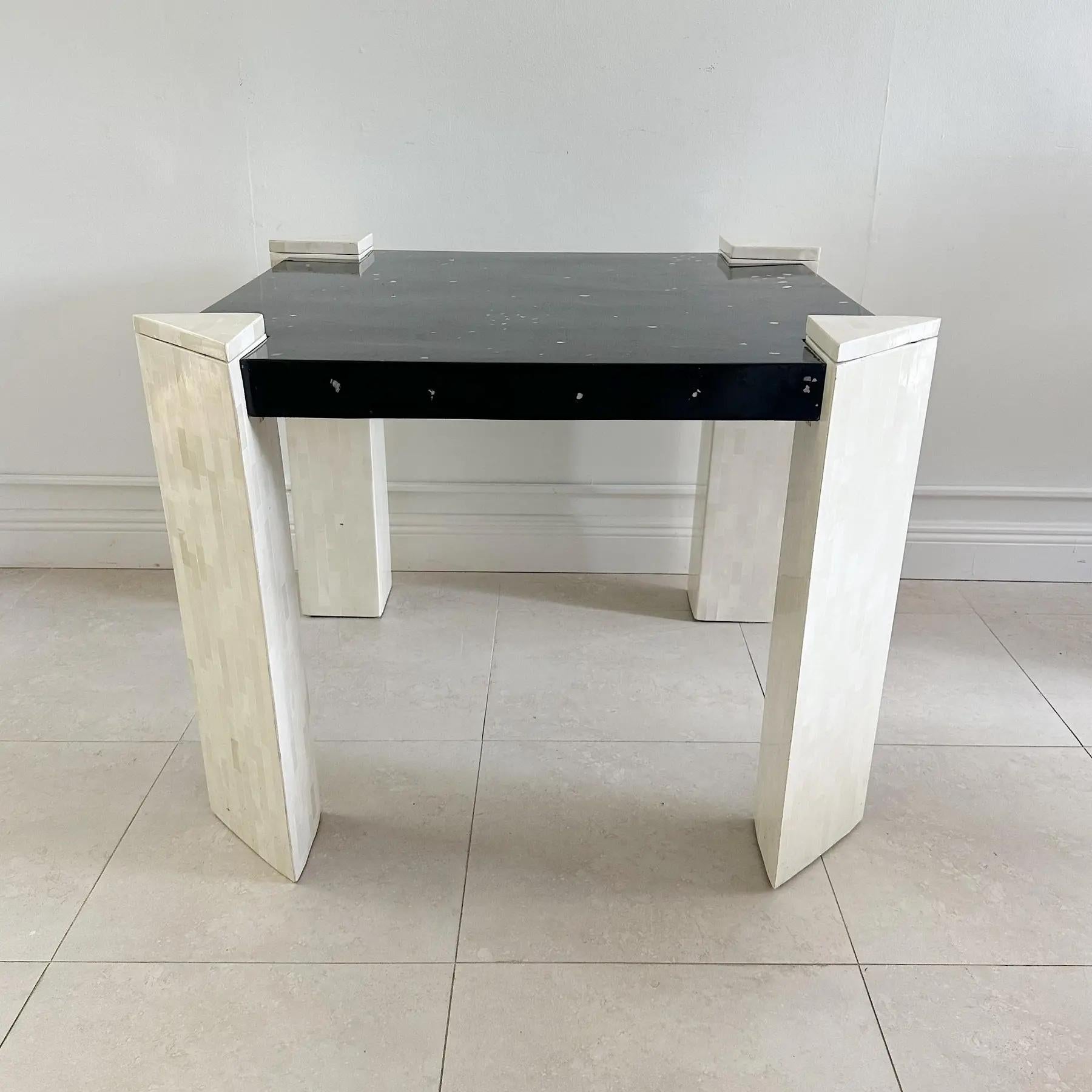 Mesa de juego de Columbia de los años 80. Patas de hueso teselado que tienen un portavasos triangular abatible. La parte superior está hecha de virutas de nácar incrustadas sobre una superficie de madera lacada en negro. El agujero de la rodilla