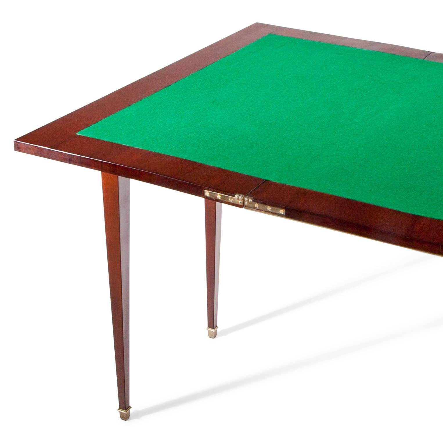 Mahogany gaming table standing on tapered feet with brass sabot. The fillings and the table edge are framed with brass moldings. The inner surface of the table is lined with green felt. Size folded out: 77 x 94 x 94 cm.