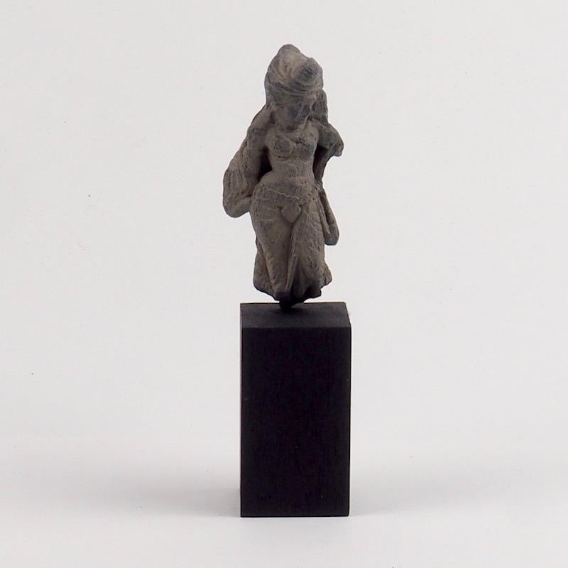 Gandharan sculpture of a female deity executed in gray schist dating from the 2nd or 3rd century
Posed in a downward gaze this figure of a sensual dancer bears her weight to her right leg with accentuated hips and exposed mid-riff. The delicate