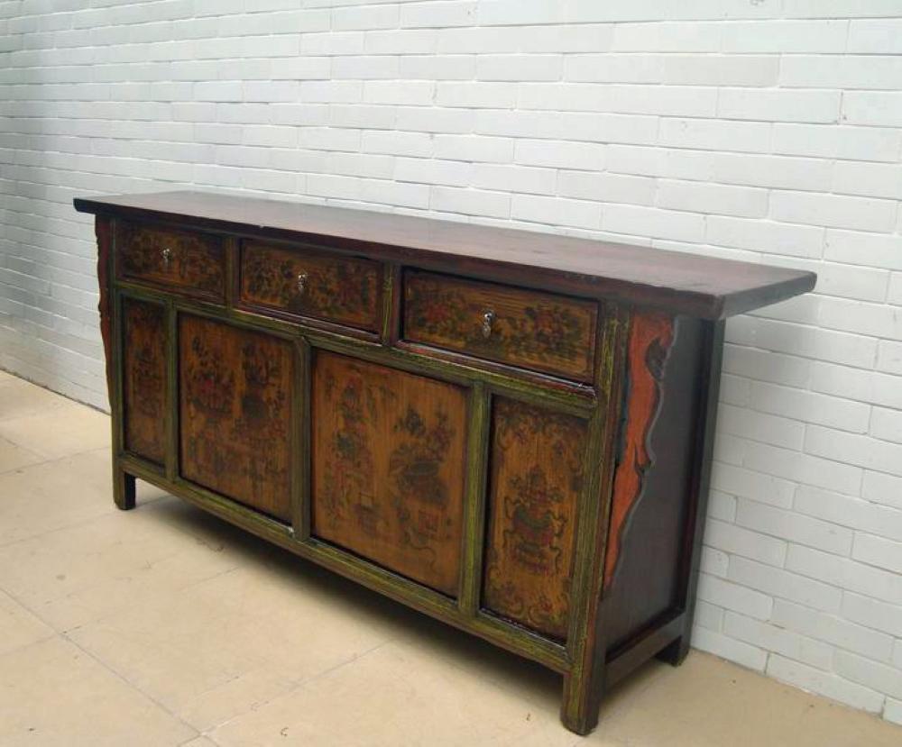 This stand out buffet sideboard boasts beautifully hand painted panel doors depicting flowers and plants in the warm muted colors of jade, amber, and crimson. A focal point are the unique carved brackets buttressing each side. There are three