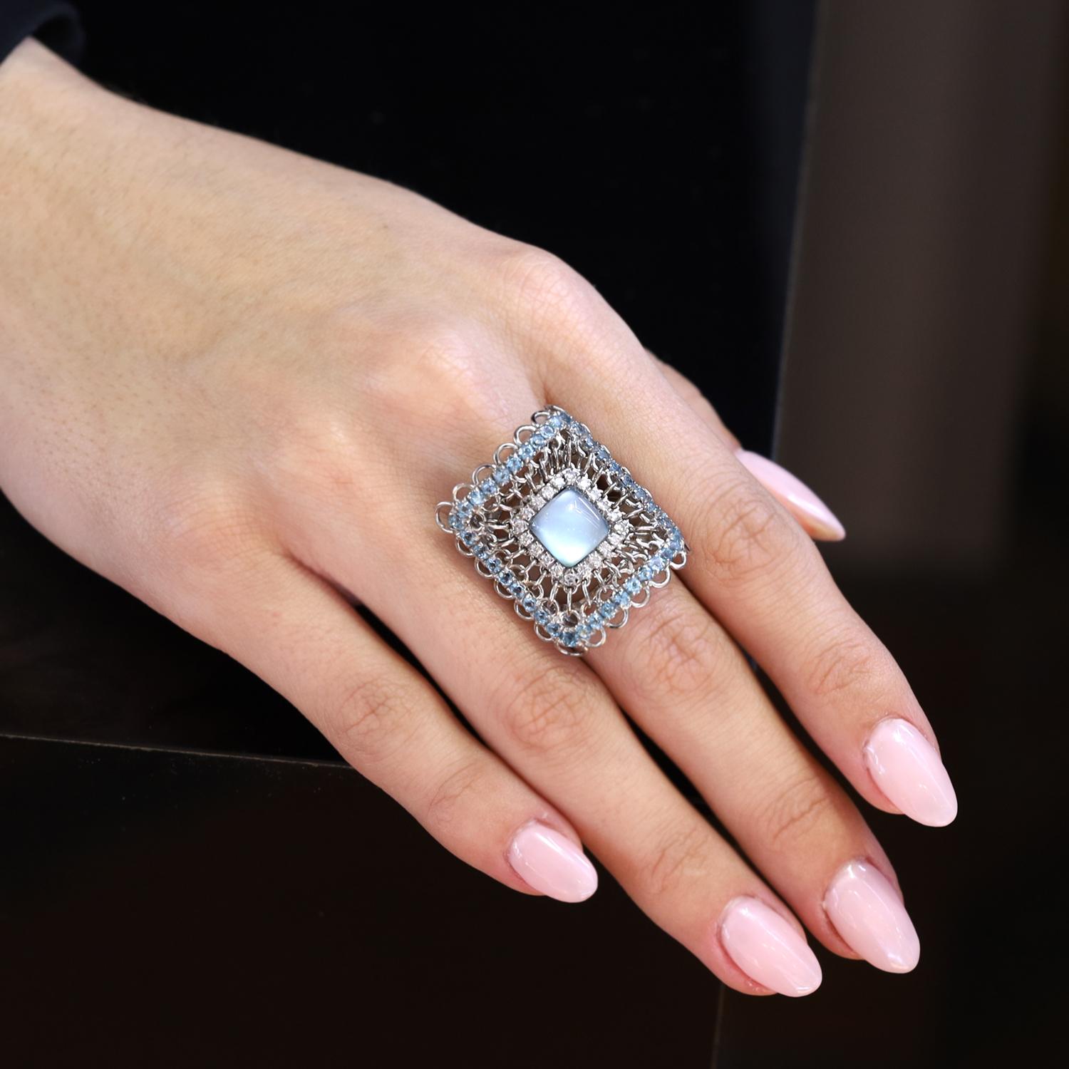 A spectacular shield shape cocktail ring centered by a smoky Aquamarine surrounded by shimmering diamonds and concentric loops and more aquamarines. Created by Italian designer Garavelli utilizing their unique technique of backing gemstones with