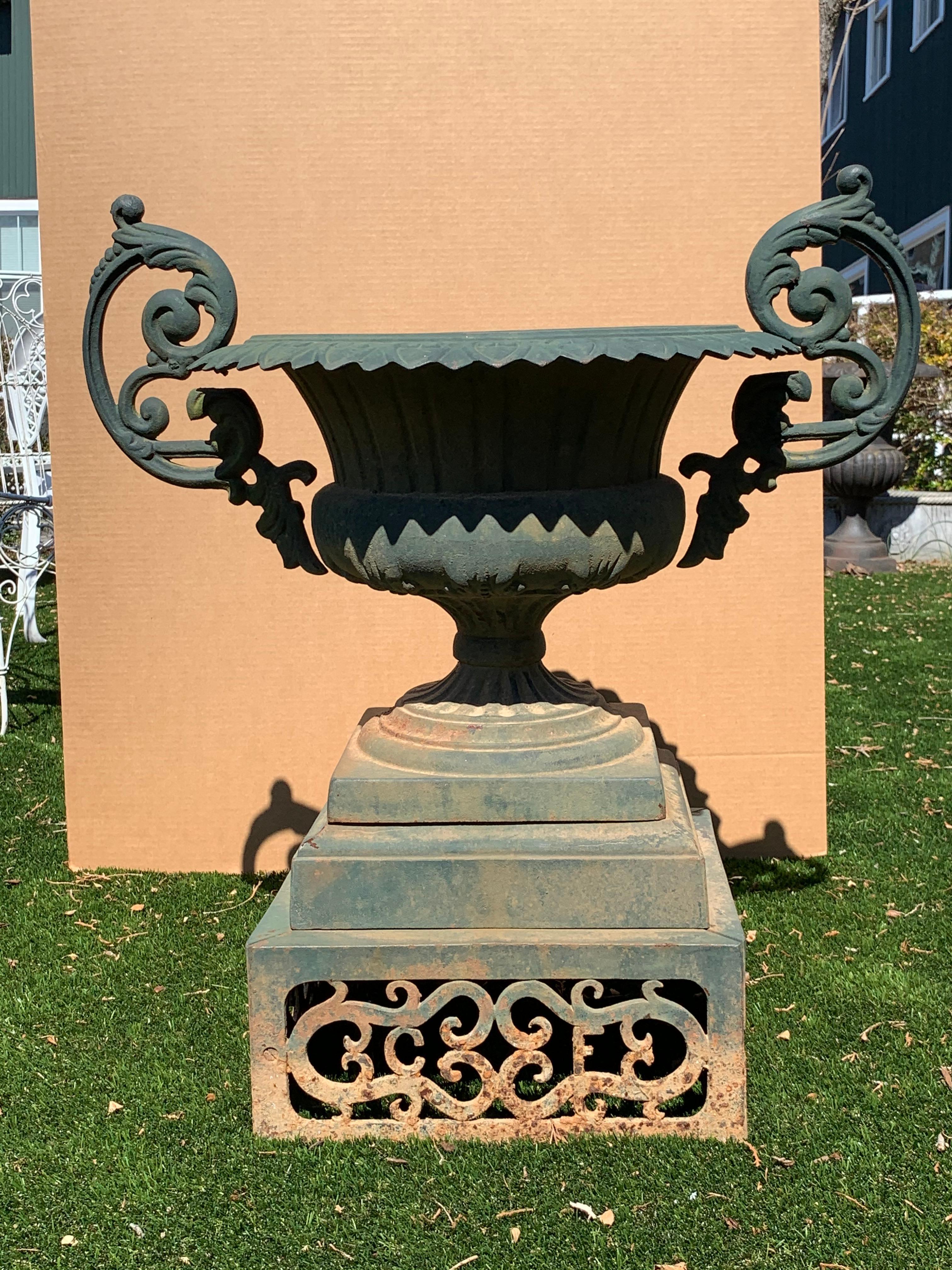 The prettiest urn in the garden, a neoclassical beauty with wonderful ribbed body, pedestal base with ornate piercework decoration on the plinth and super fancy handles on each side. The color is an enviable natural aged verdigris with contrasting