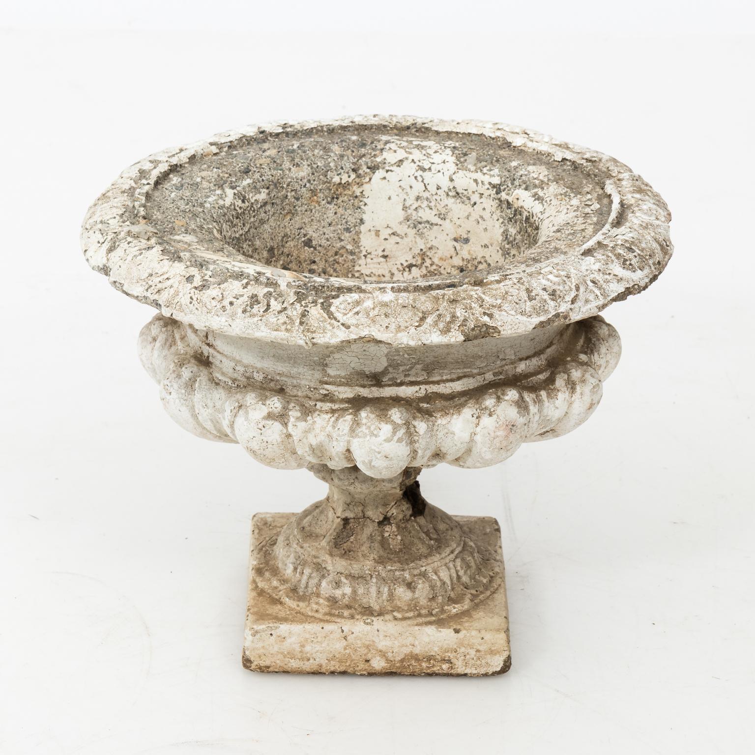 Circa 20th century Garden cement urn with egg-and-dart detail on a square pedestal. Please note of wear to age due to exposure to the elements along with damage to the stem of the urn causing cracks and minor loss.