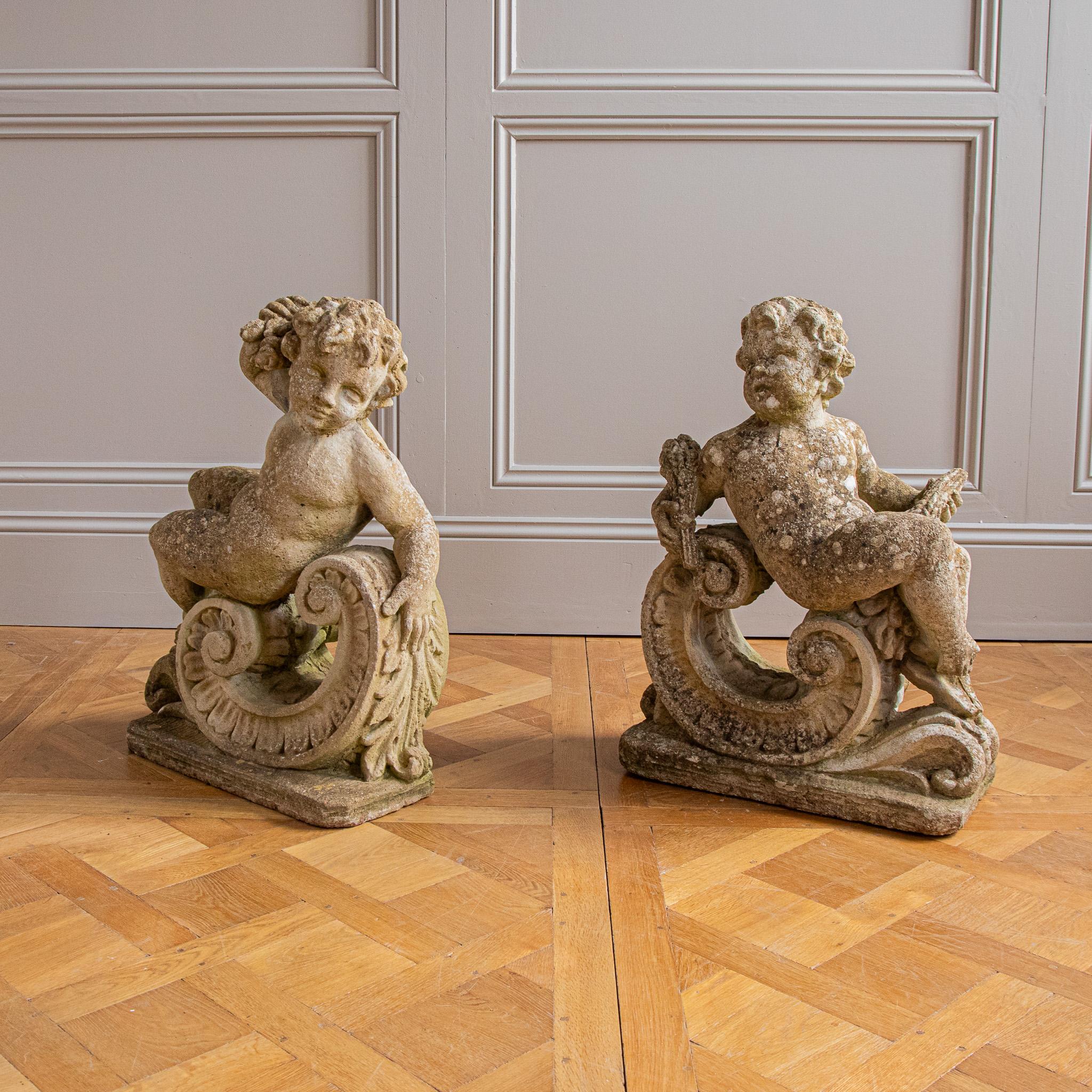 Coppia di modelli di composizione in pietra di putti reclinati, in stile rococò, XX secolo, probabilmente raffiguranti l'Estate e l'Autunno, modellati come opposti, ciascuno reclinato su un cartiglio foliato modellato, che reggono rispettivamente
