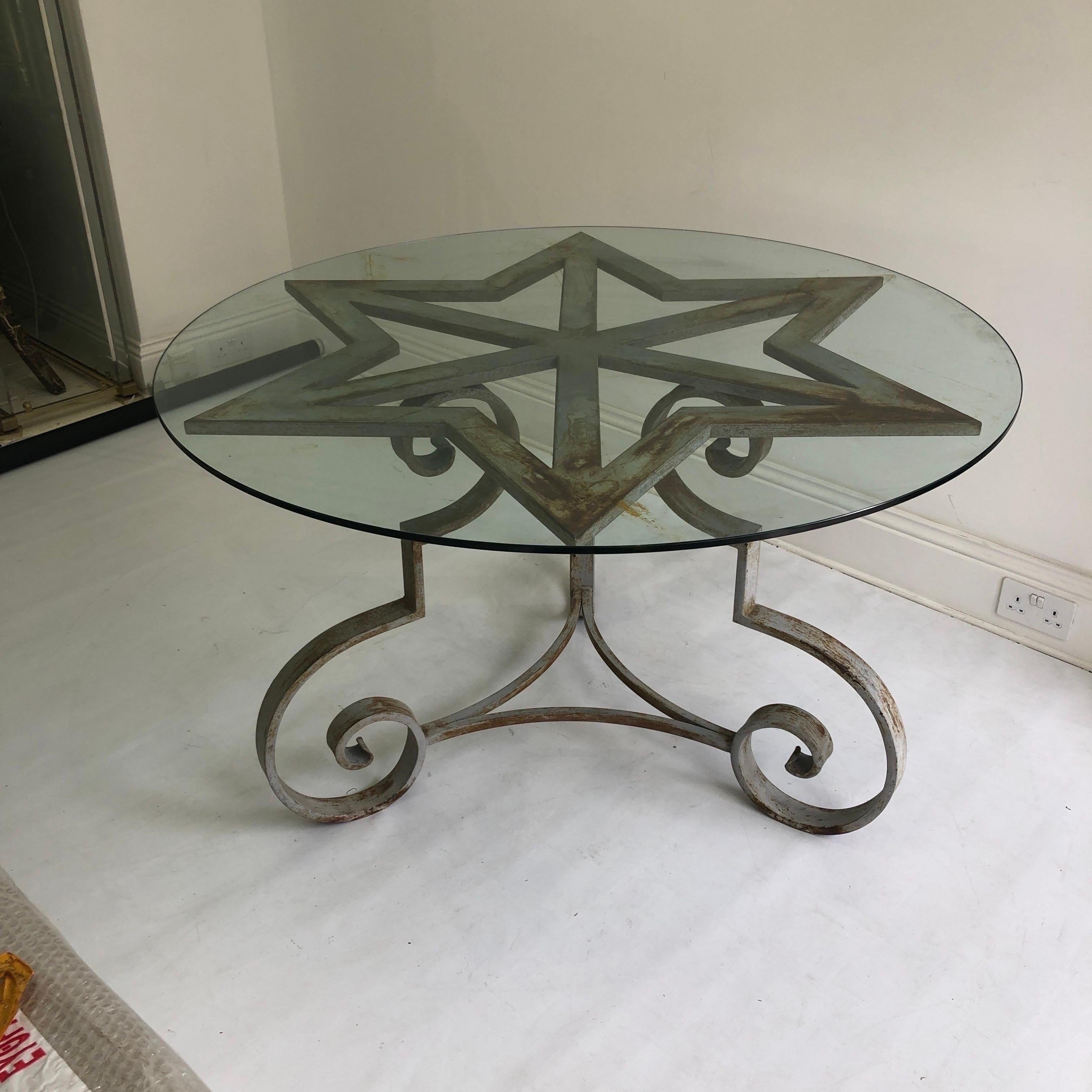 An amazing distressed star-shaped dining table made of pure cast iron. Fantastically angular, this sturdy table is completed with a round glass top. Three swirling feet, with touches of the neoclassical, support the six-pointed star. 
Due to the