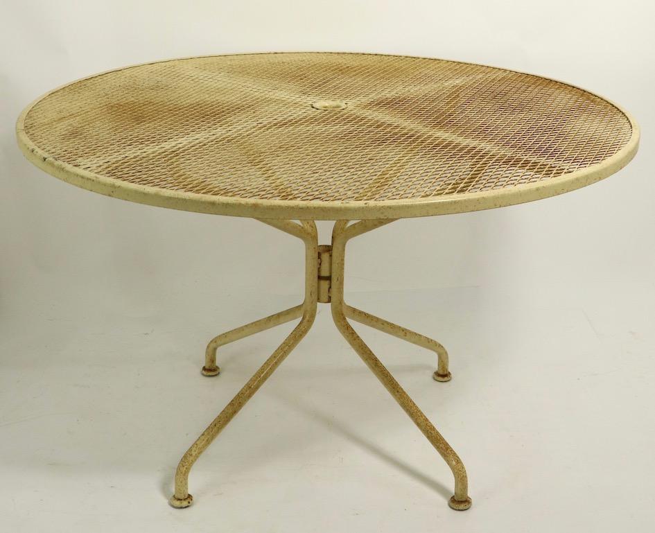 Nice garden, patio dining table, attributed to Woodard. The table has a metal mesh top, with curved tubular legs, it is in original tan, yellow paint finish which shows cosmetic wear, normal and consistent with age. The top features a center hole