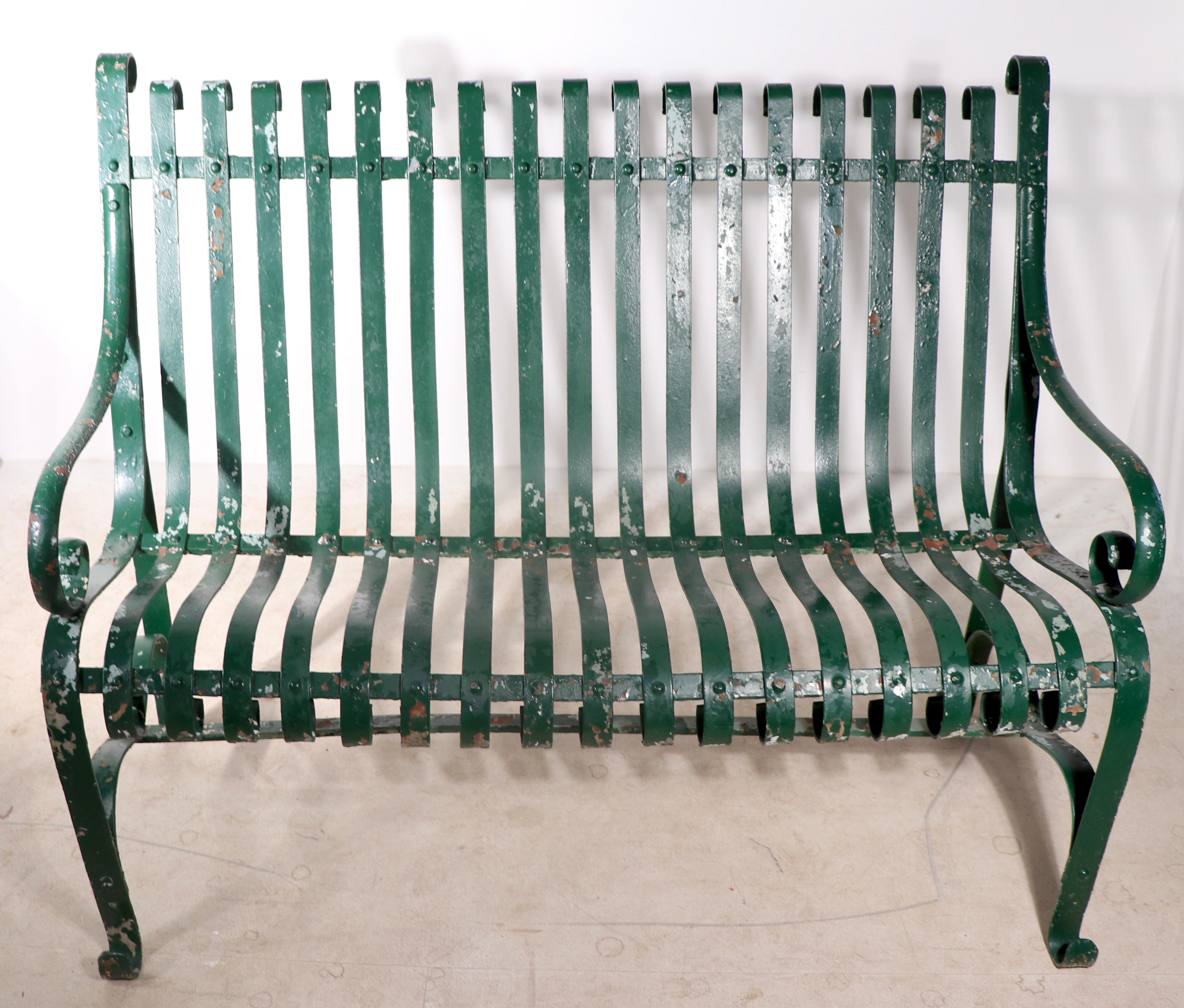 Charming garden, patio, or park loveseat size bench of wrought iron and strap steel. This example is in very good estate condition, sturdy, s and solid,  showing only cosmetic wear to the paint finish, normal and consistent with age and use. 
 Hard