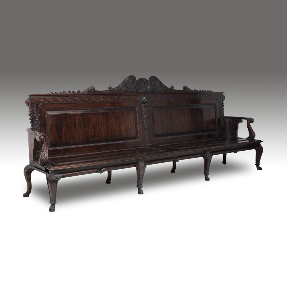 A fine pair of William Kent design carved teak or mahogany garden or hall benches. Each paneled back centered by a scrolling scallop shell crest above a mask with Vitruvian scroll frieze above solid paneled seats with acanthus scroll arms on