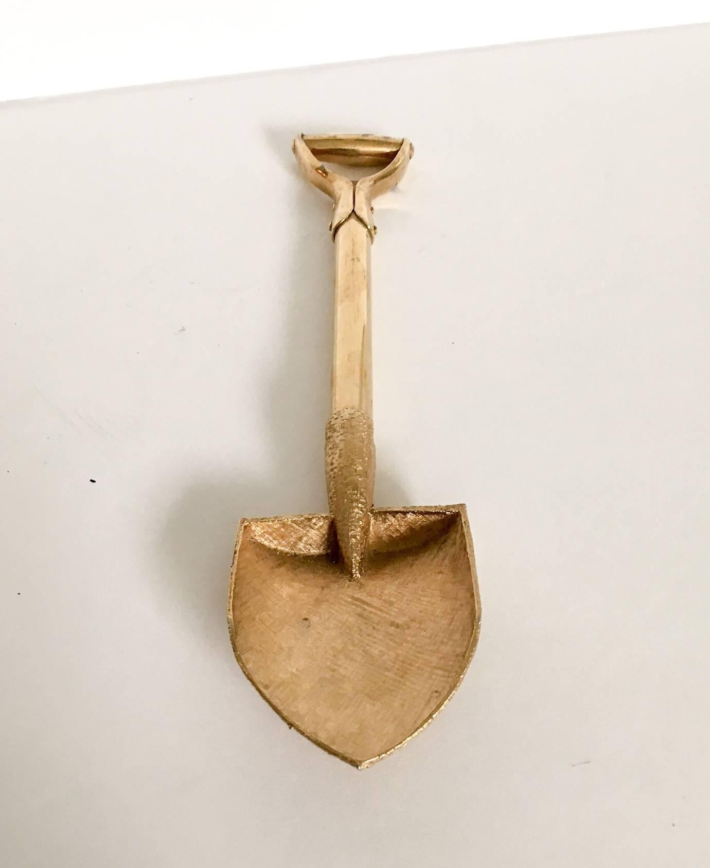 Delightful brass handle with detailed gold tone garden shovel bottle opener. Note the riveted detail at the spade handle and the crosshatch pattern on the spade point. The bottle cap opener is under the spade handle. Unmarked; circa 1950s. Equally