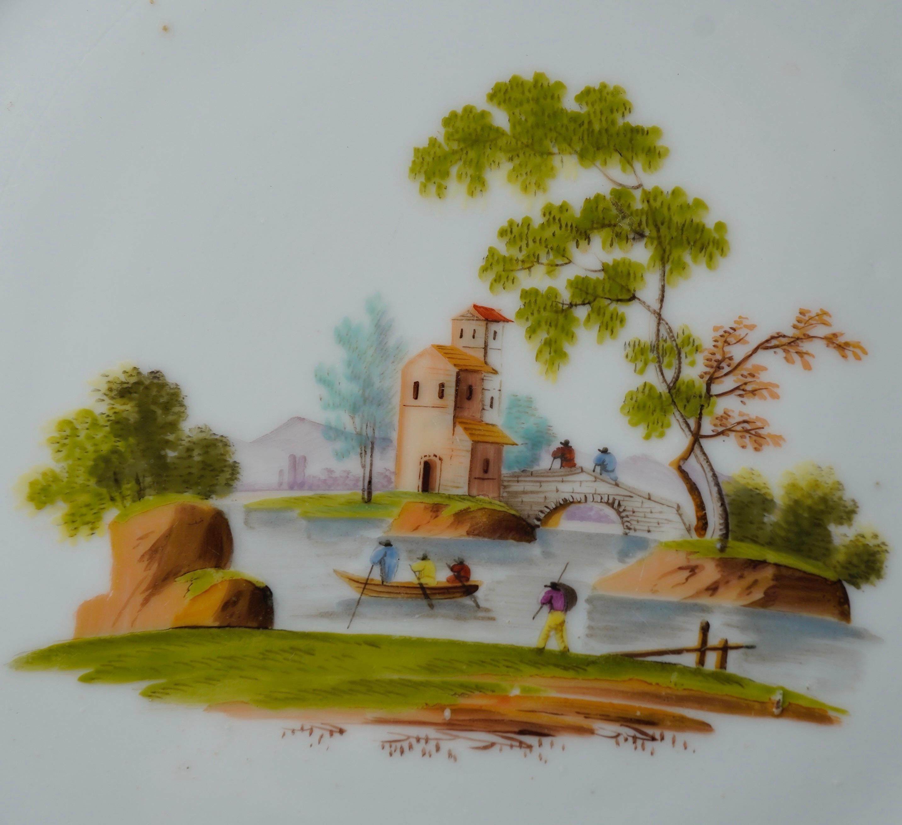 Gardner of Moscow Russian Porcelain plate, painted with a landscape, with a bridge leading to a building in a wooded landscape, several figures wandering around, within a simple gold band and rim. 
'C' maker in underglaze blue, 
also incised '23',