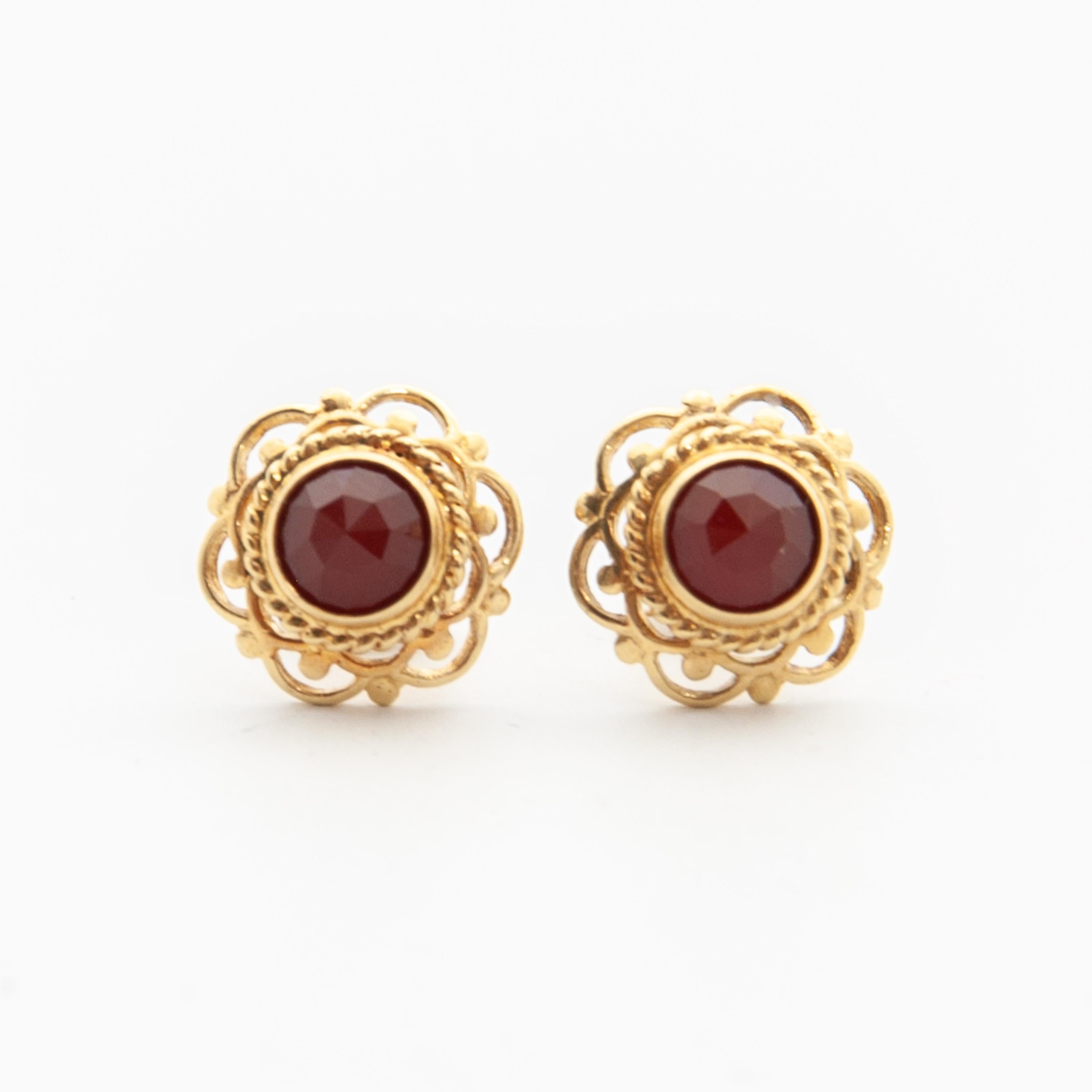 Elegant pair of faceted red garnet stud earrings set in a solid 14 karat yellow gold mounting. These beautiful studs have a very fine gold lacy border which looks lovely. The inner side has a rope motif around the center garnet, while the outside of