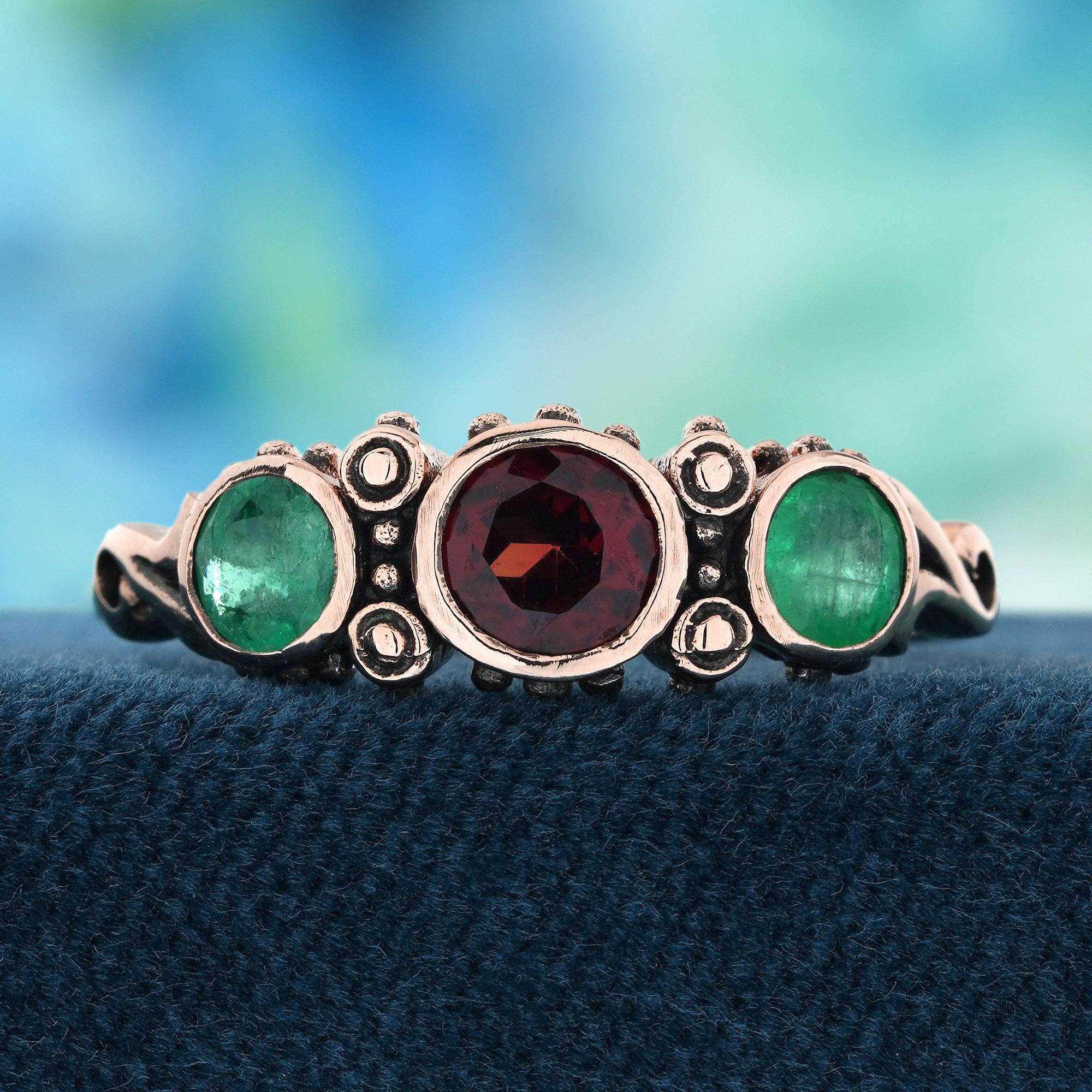 Three captivating garnets, each set at the center of the design, creating a bold and beautiful focal point. Between each garnet, two vibrant emeralds delicately separate them, adding a stunning contrast of color. The intricate filigree detailing