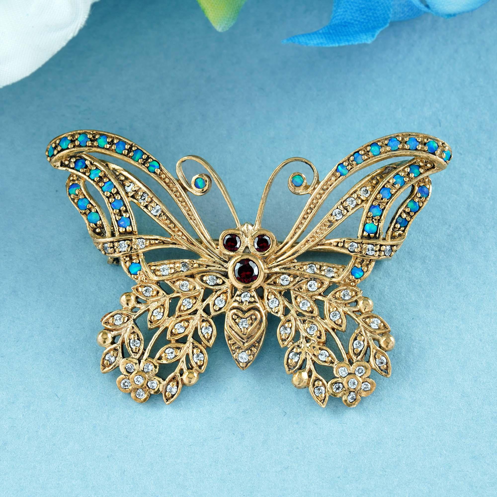 This stunning gold butterfly brooch in vintage style highlights an open-winged butterfly featuring red round garnets for the head and eyes to catch the attention, green round opals for the antenna, and embellishments of both on the inner and outer