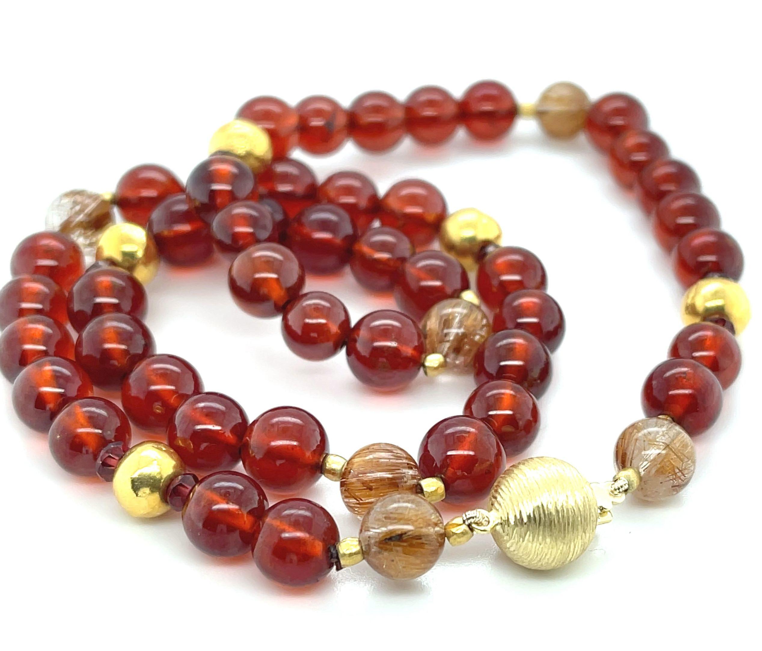 Questa collana ricca e colorata è caratterizzata da perle di granato rosso di qualità insolitamente fine disposte con perle di quarzo rutilato e accenti in oro giallo 18k. I granati da 8 mm hanno un'incantevole trasparenza e un colore rosso arancio