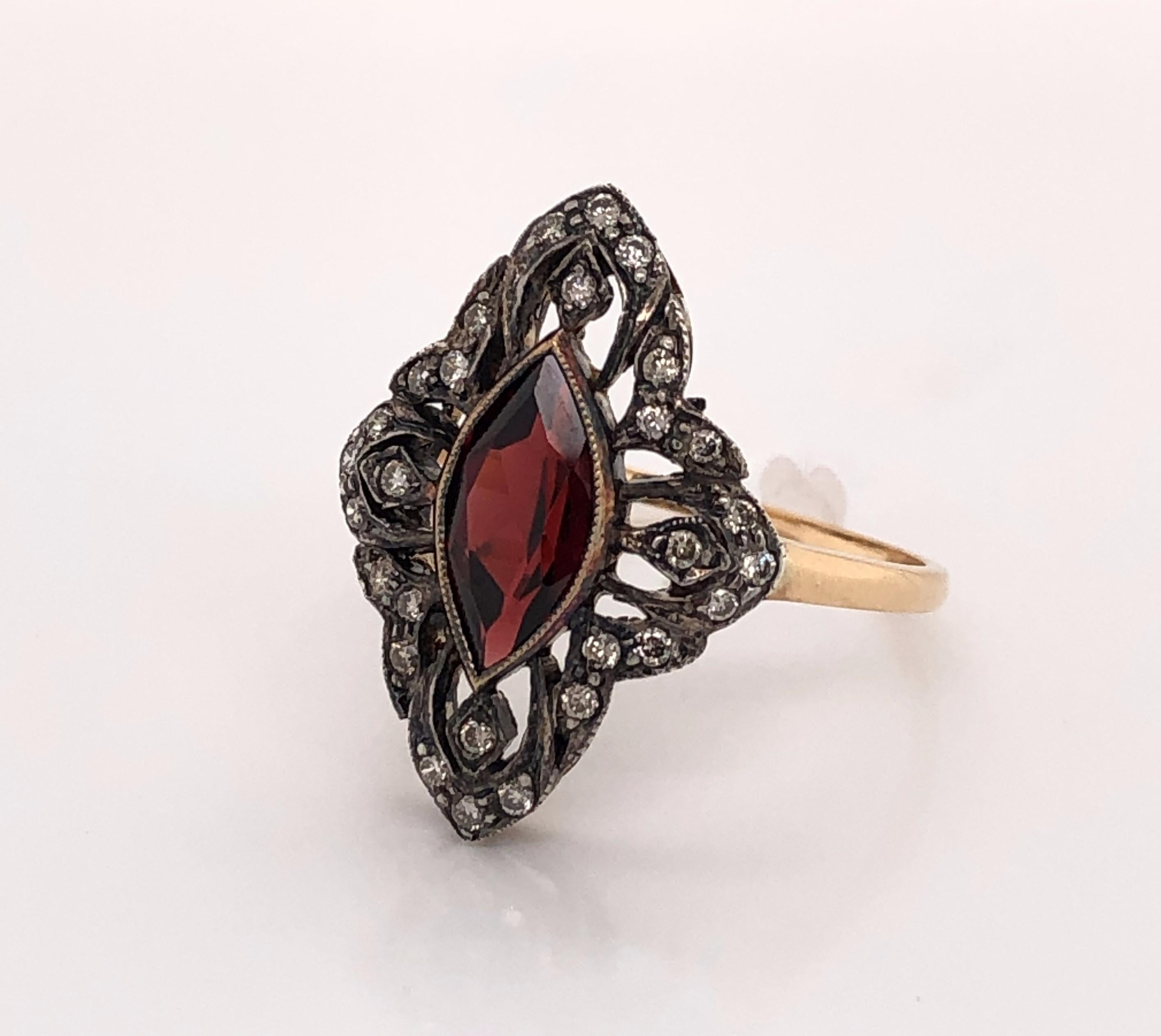 A beautiful rich red marquis cut garnet gemstone is the focal point of this elegant ladies antique ring. Rose cut diamonds adorn the lacy filigree in eighteen karat (18K) rose gold and create an ornate frame around the center stone. In size 7.5. In