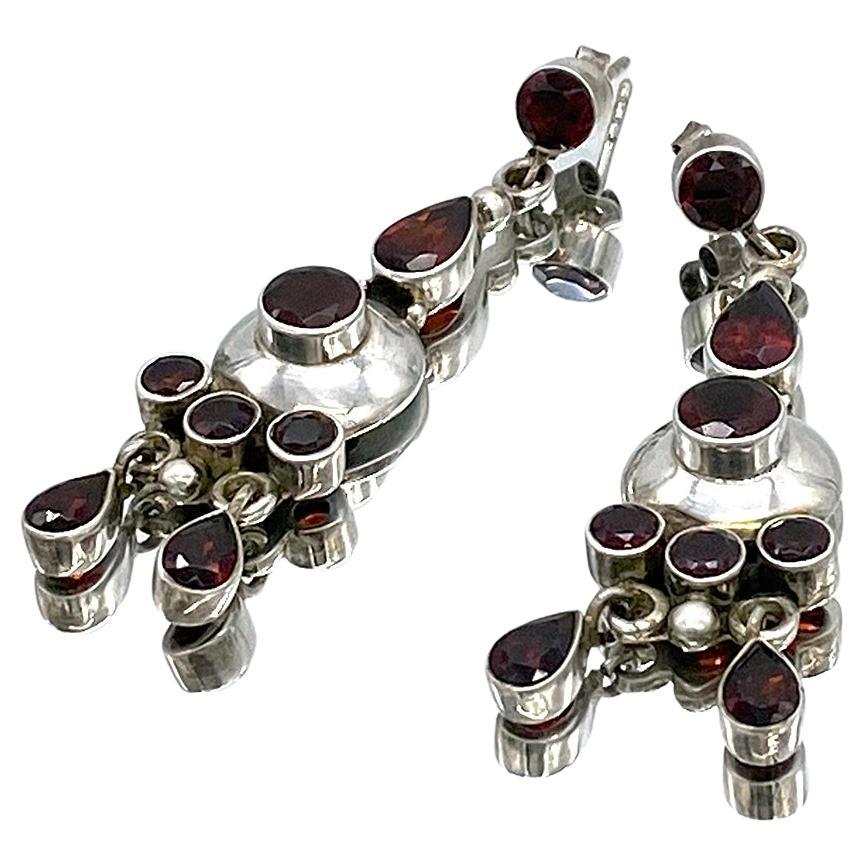 Si tratta di un paio di orecchini in argento sterling con gemme di granato lavorate dall'artista in studio. Questi orecchini pendenti sono costituiti da gemme di granato taglio rosa e taglio pera incastonate su montature in argento sterling aperte