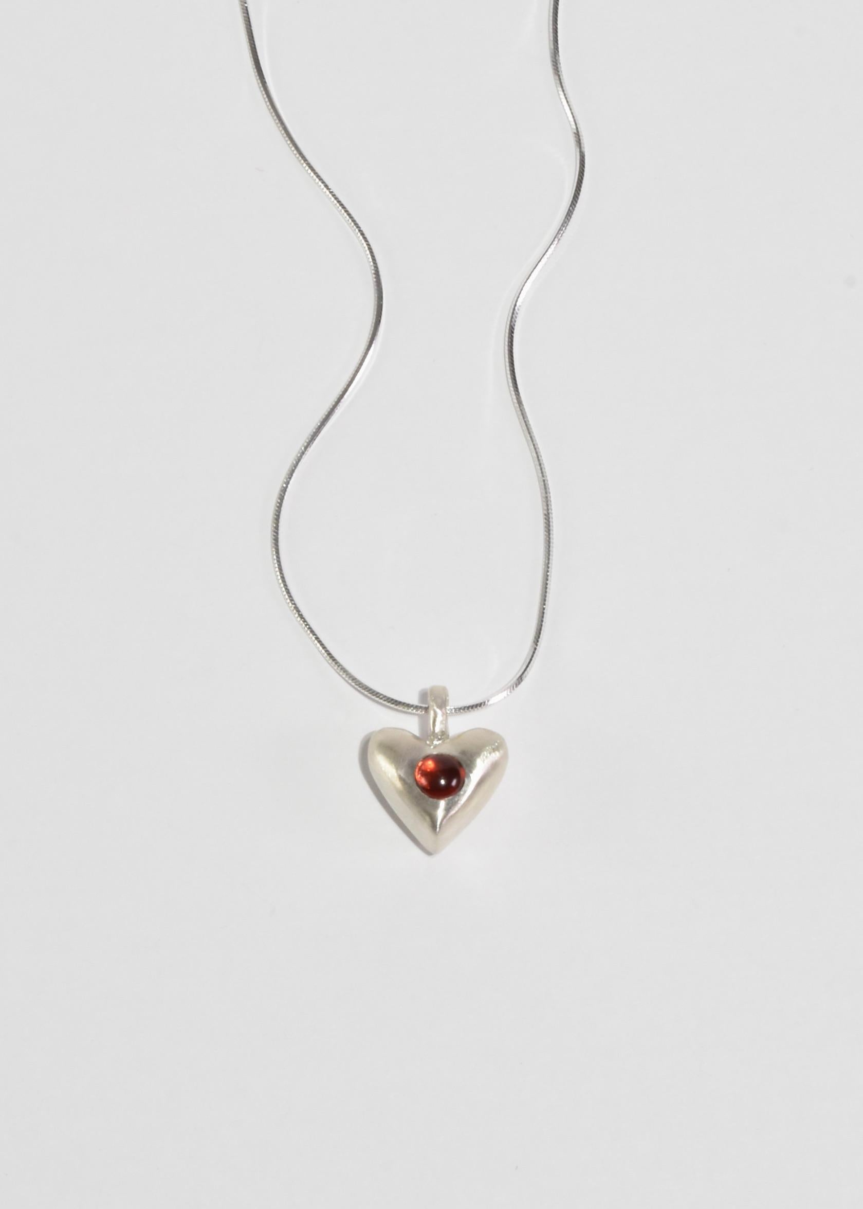 Collier en argent avec un pendentif en forme de cœur et des détails en grenat. Fermeture à boucle. Inspiré par les représentations du cœur telles qu'elles apparaissaient dans les premiers arts décoratifs américains.

Chaque pièce est sculptée,