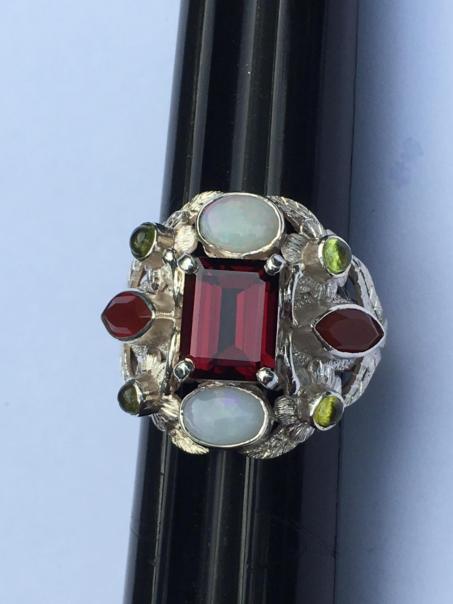 This ring is not just a ring its piece of art. Center red stone is  7 X 9 MM very clean Garnet, 6 X 8 MM oval Opal, 3 X 6 MM Marquise Carnelian and 2 MM Round  cab Peridot.
This ring is created by very skilled gold and silver smith named. R.Rasile