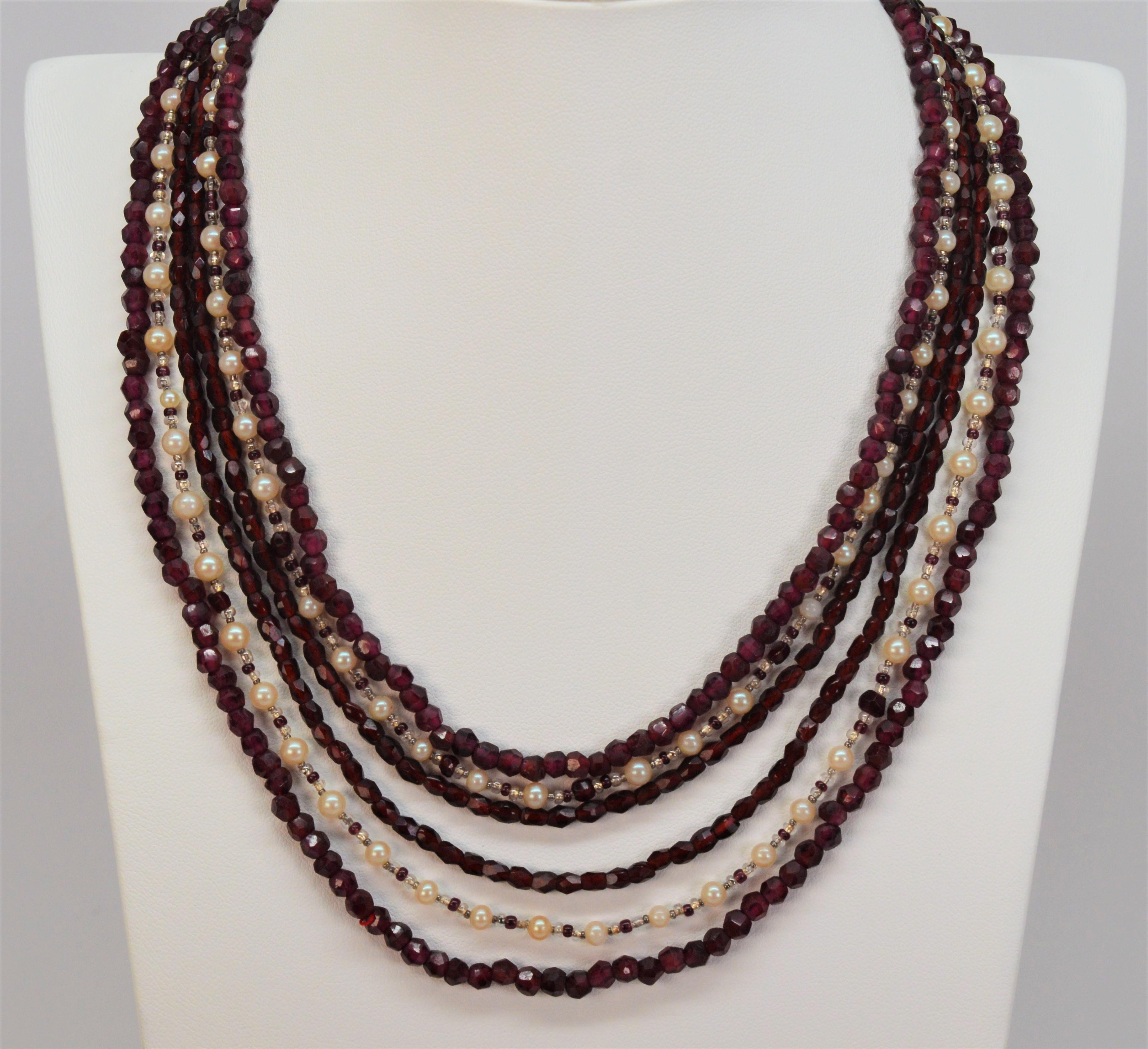 Jeweled with a floral inspired garnet floret atop beautiful 10 karat gold leaf and vine filigree, this antique clasp creates a stunning focal point for this gorgeous multi-strand beaded garnet necklace. This estate piece has six graduated lengths