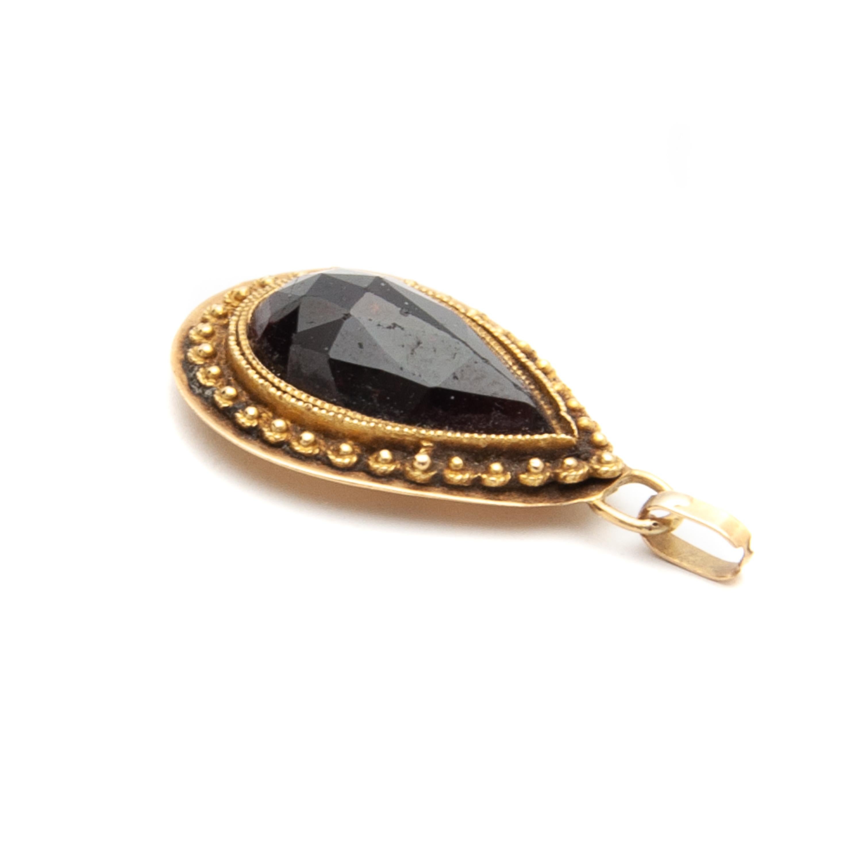 This is an antique drop-shaped garnet pendant created in a 14 karat yellow gold frame. The garnet is surrounded with a double ribbed border and the outer edge has a cannetille design with small knots, the so-called 'spiders'. Cannetille typically
