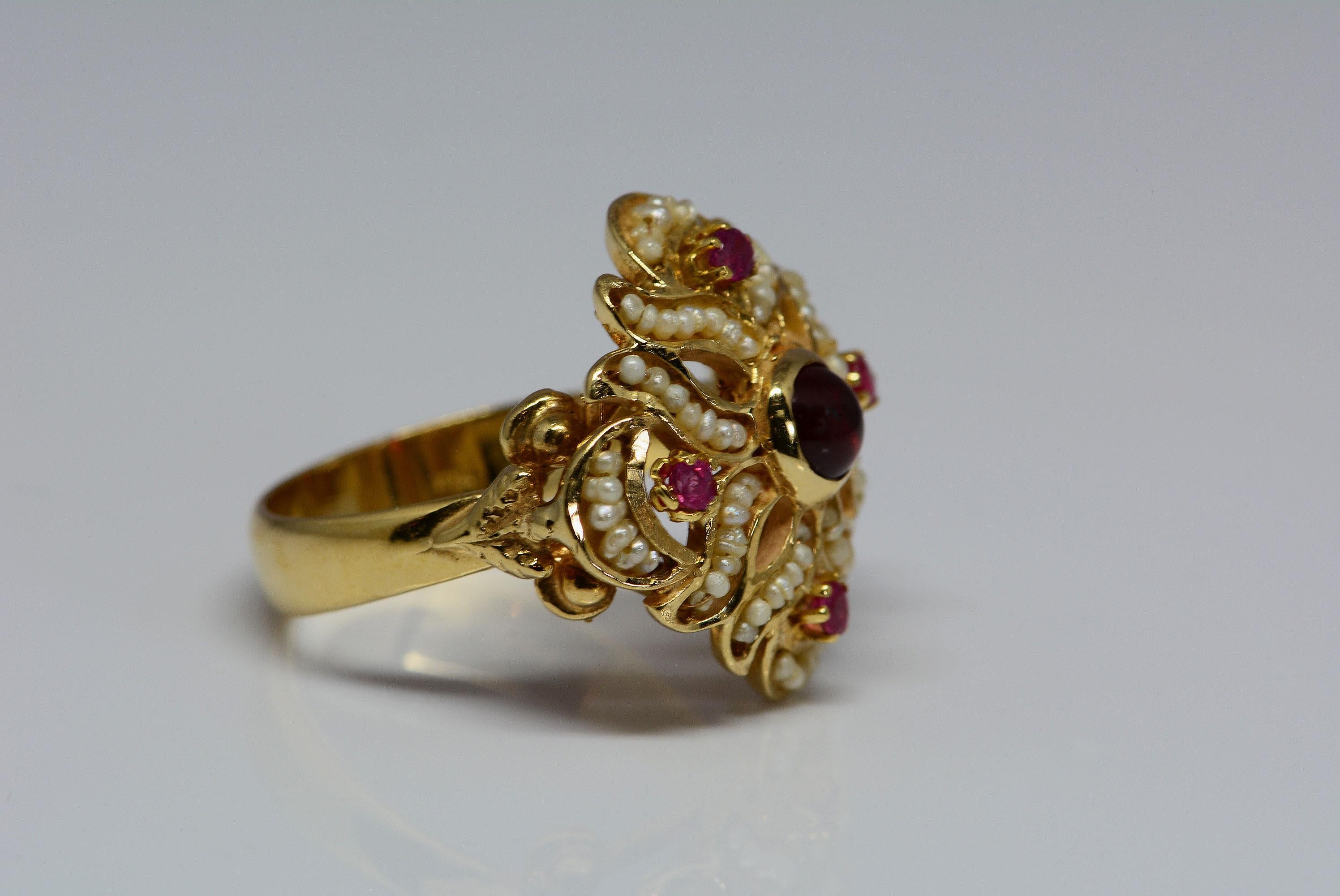 
This ring reminds us of something you would see in the tudor time period, with the combination of the red rubies, cabochon cut garnet, and seed pearls.
The ring was handmade in Italy and is made from 14 karat yellow gold.

The center gem in this