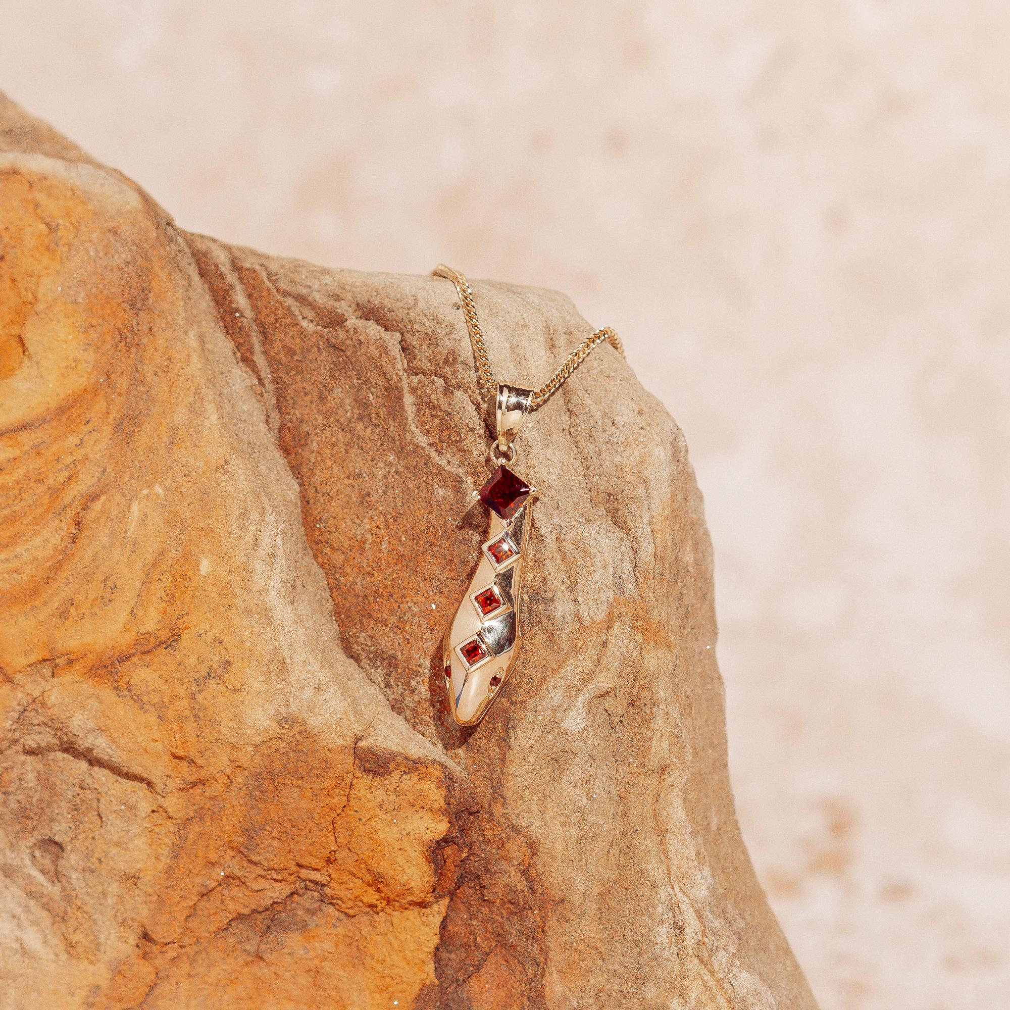 Realizzato in oro giallo 14 carati, questo esclusivo ciondolo a forma di testa di serpente ha una leggera curva che gli conferisce movimento. È impreziosito da granati graduali con taglio a principessa e occhi tondi in granato. Sospeso da una catena