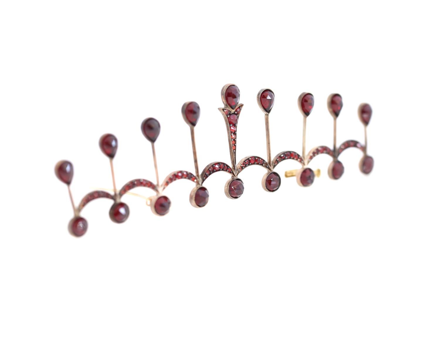 A Garnet Brooch depicting tiara or a crown. Silver with Gold, a technique used at that time. Collectable jewelry from the early 20th century. 
Garnet is known to be a stone of the month of January. Very deep red color. It is an amazing opportunity