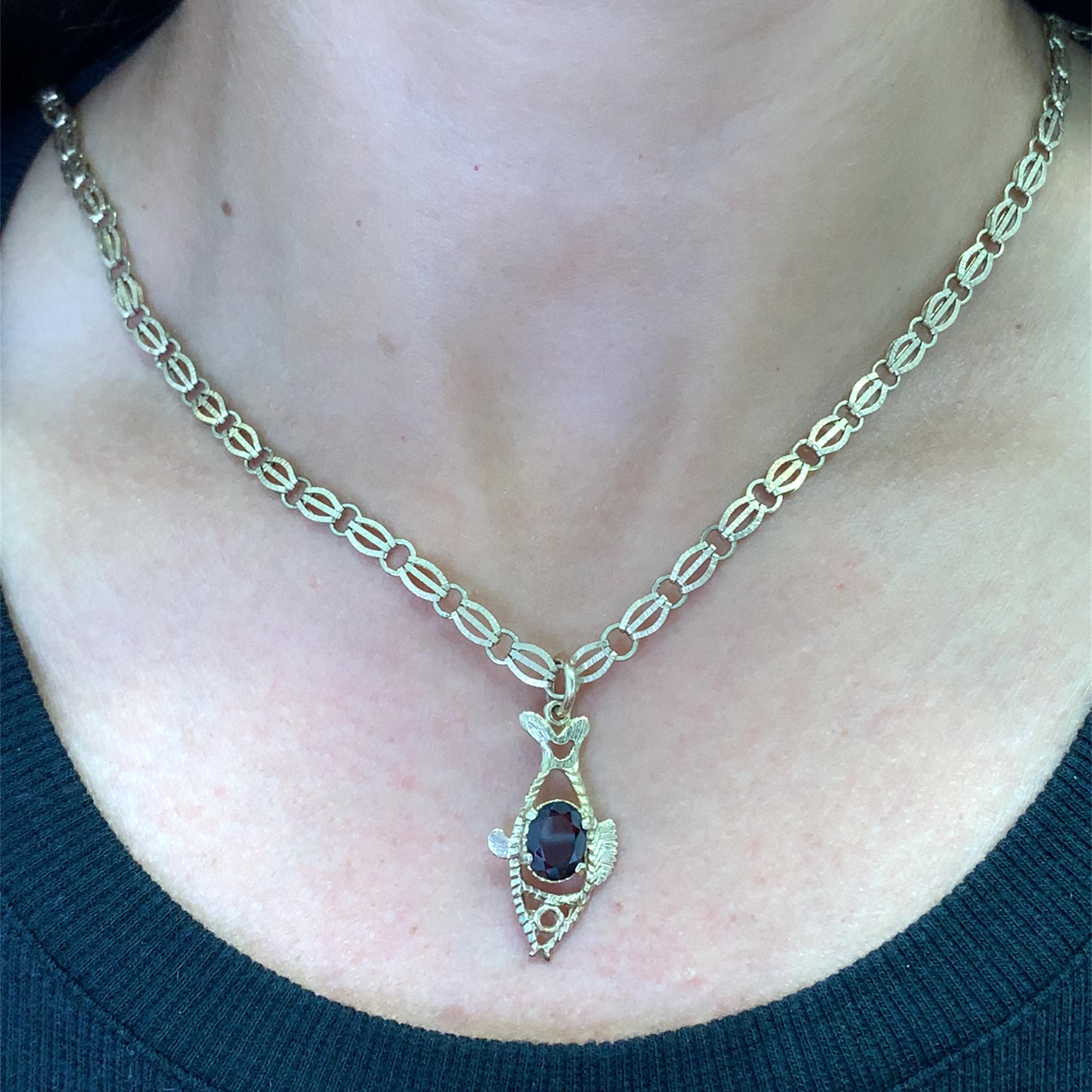 Elevate your style with this exquisite 9ct yellow gold charm necklace. The pendant features a mesmerizing oval garnet, radiating a deep red hue. Its smooth, polished surface reflects light beautifully. This vintage fish shaped charm necklace is a
