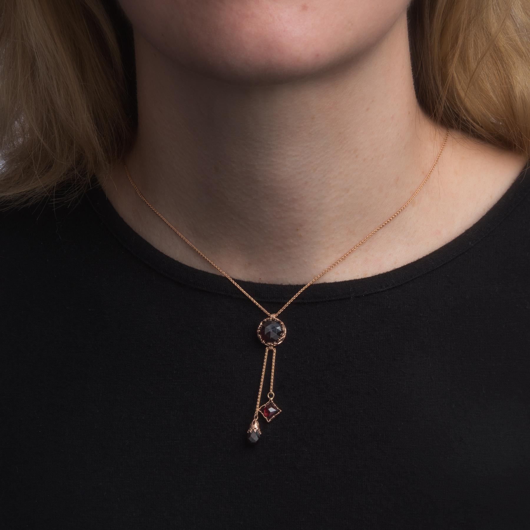 Finely detailed garnet drop necklace, crafted in 14 karat rose gold.  

Checkerboard faceted round cut garnet measures 10mm (estimated at 5 carats), accented with two 5mm garnets (lower) that are estimated at 1 carat each. The total garnet weight is
