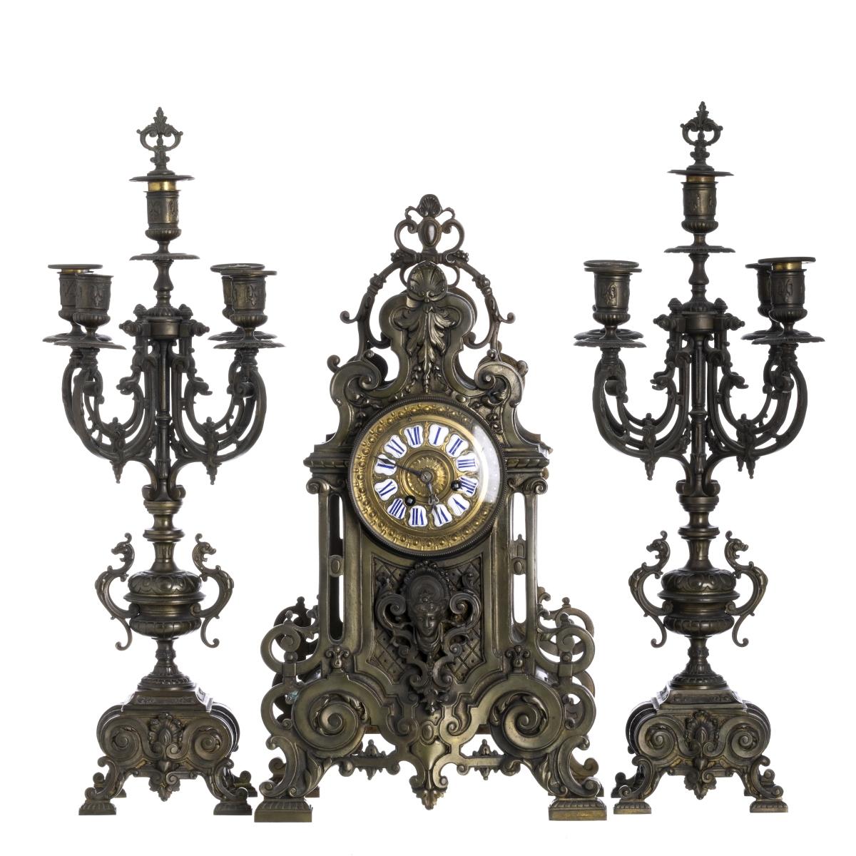 This elegant garniture set, composed of a central clock and a pair of matching candelabra, was created in 19th-century Europe and reflects the refinement and decorative taste of the period. The clock, crafted in richly finished yellow metal,