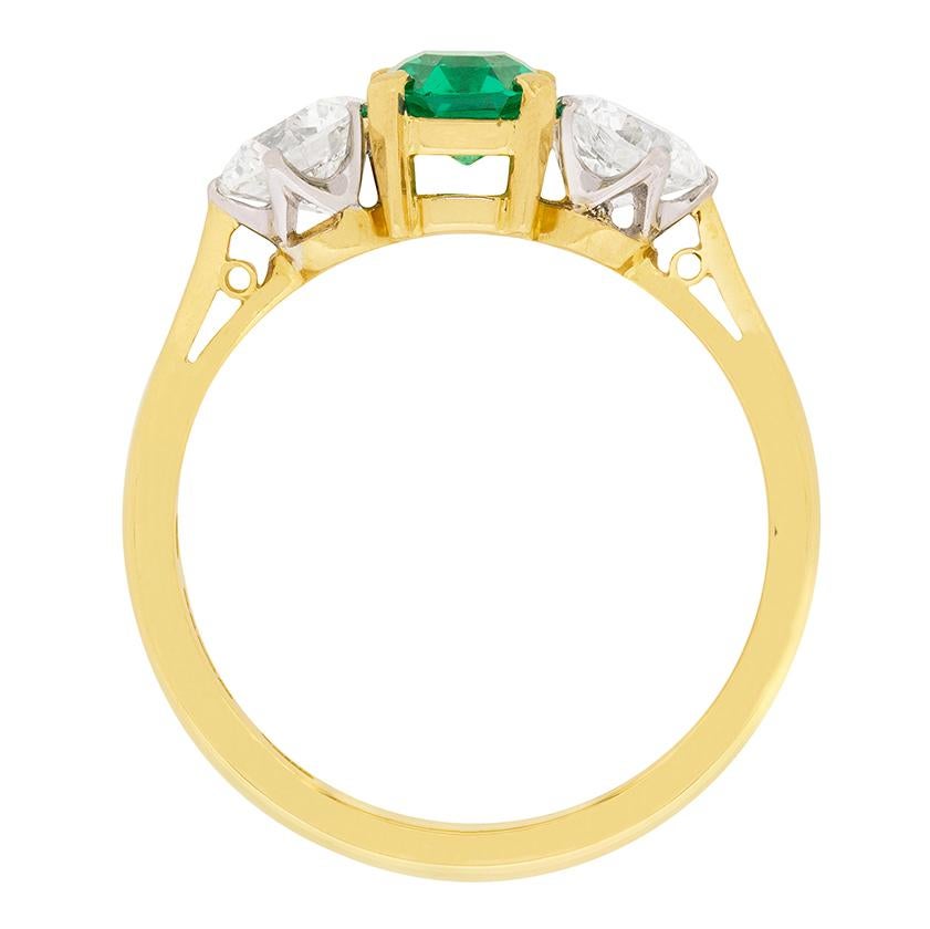 This vintage Garrard ring features a stunning green emerald in the centre, supported either side by two shining diamonds. The natural emerald weighs 1.10 carat and is claw set by the corners using 18 carat yellow gold claws. The two diamonds, which